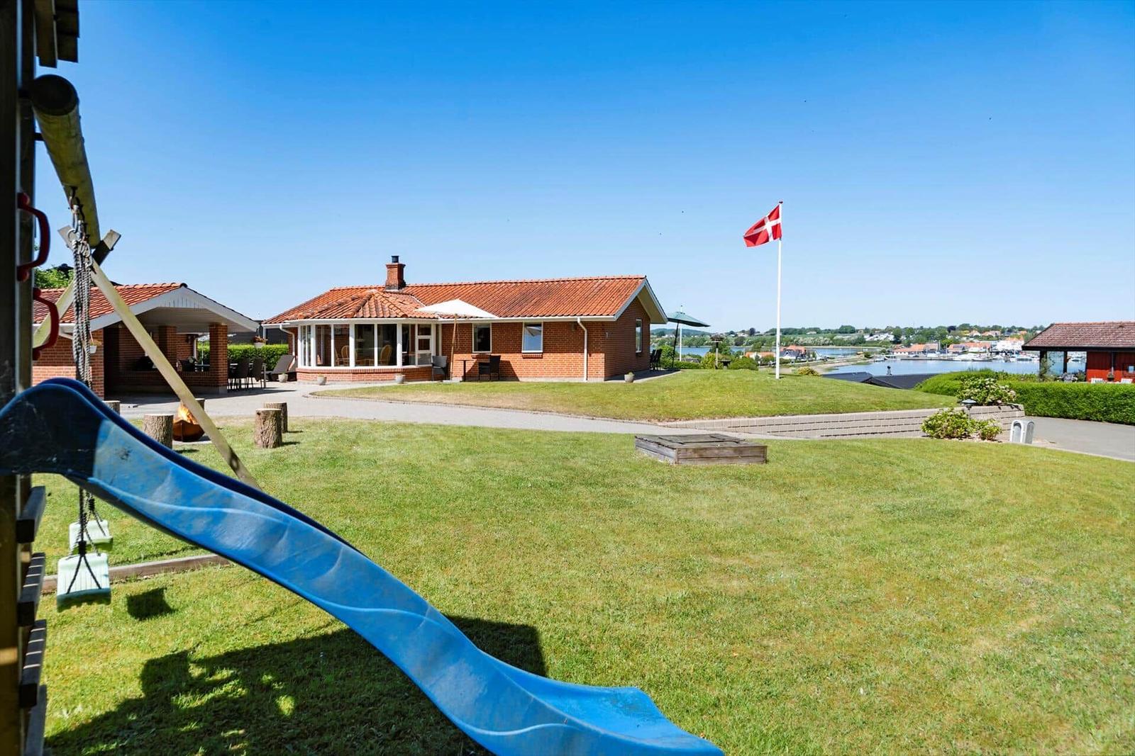Rotes Haus mit Terrasse, Flagge und grünem Garten. Blick auf Wasser und Hafen.