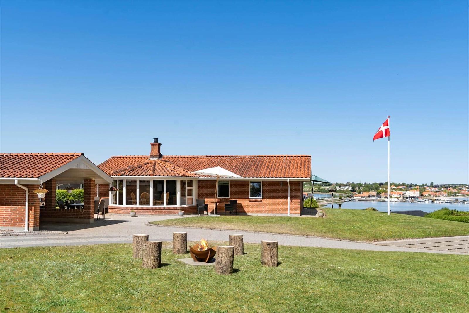Haus mit Terrasse, Grillplatz und Blick auf Hafen mit dänischer Flagge.