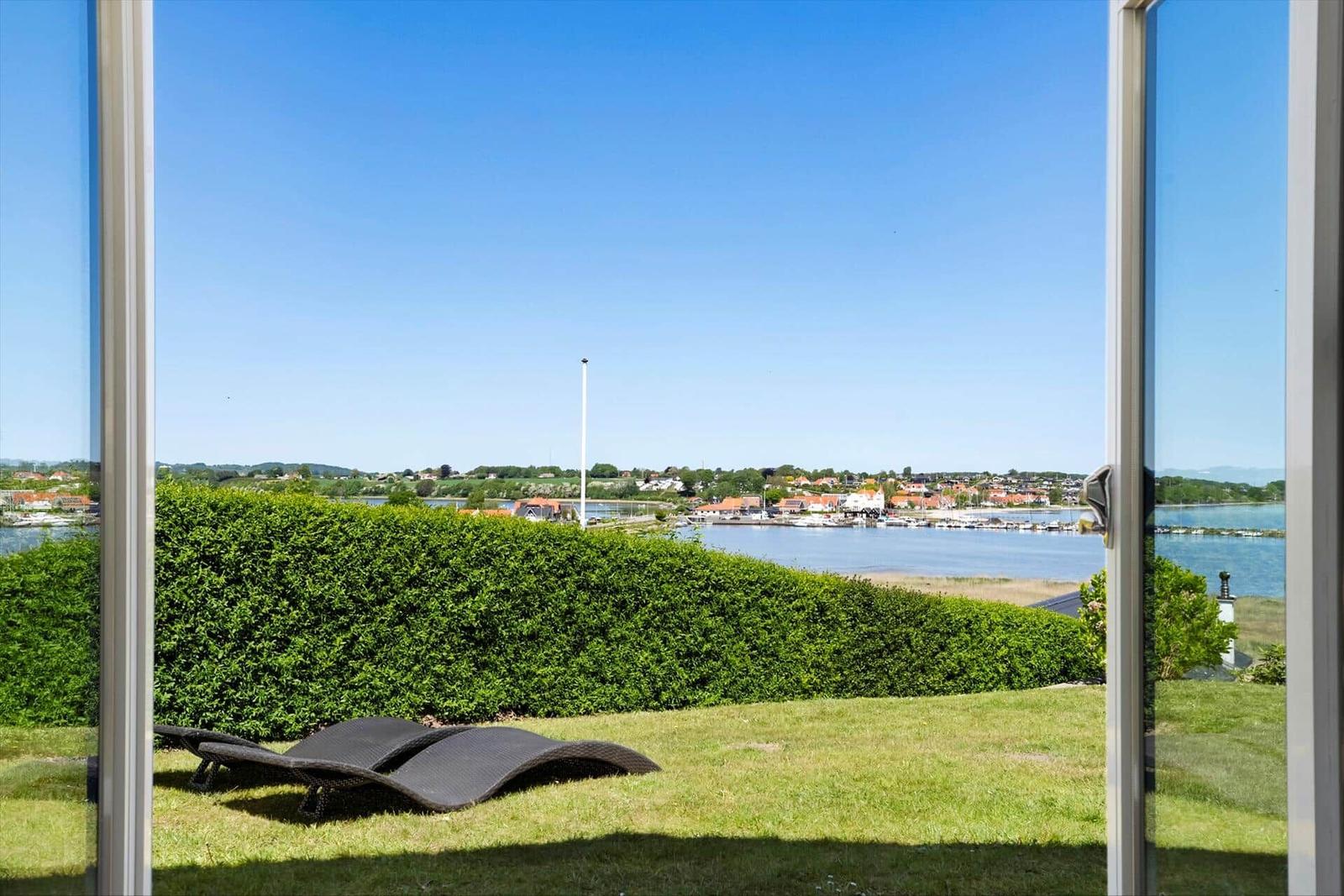 Durch die Glastüren blickt man auf einen grünen Rasen mit Liegestühlen und einen Hafen mit Booten.