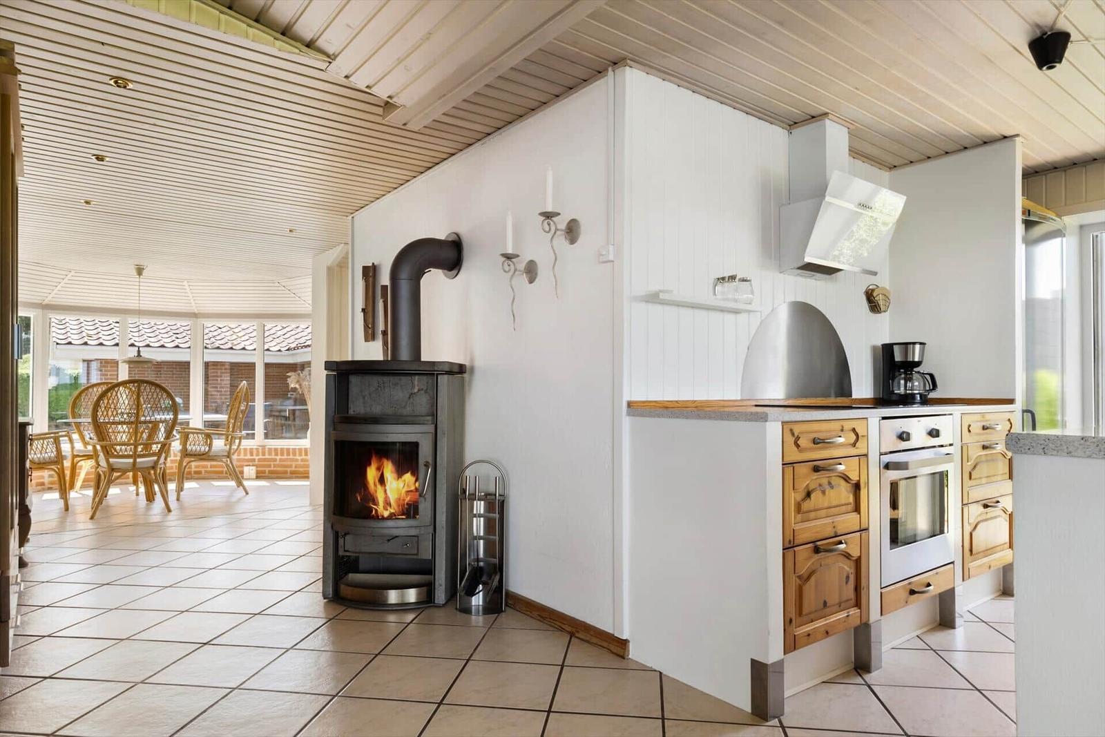 Küche mit Holzschränken und Kaminofen im Hintergrund.