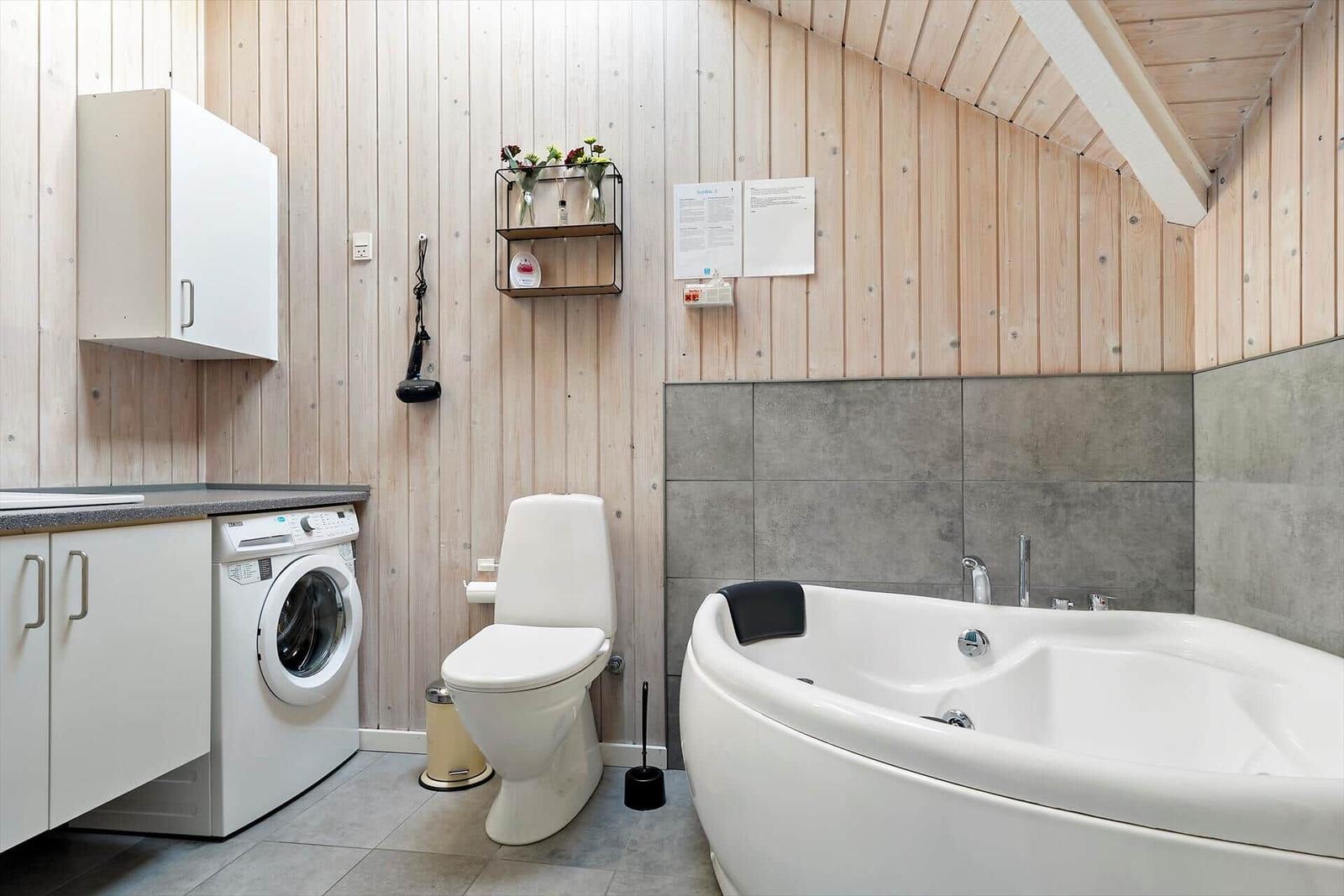 Bathroom with bathtub, toilet, and washing machine. Wooden wall and concrete tiles.
