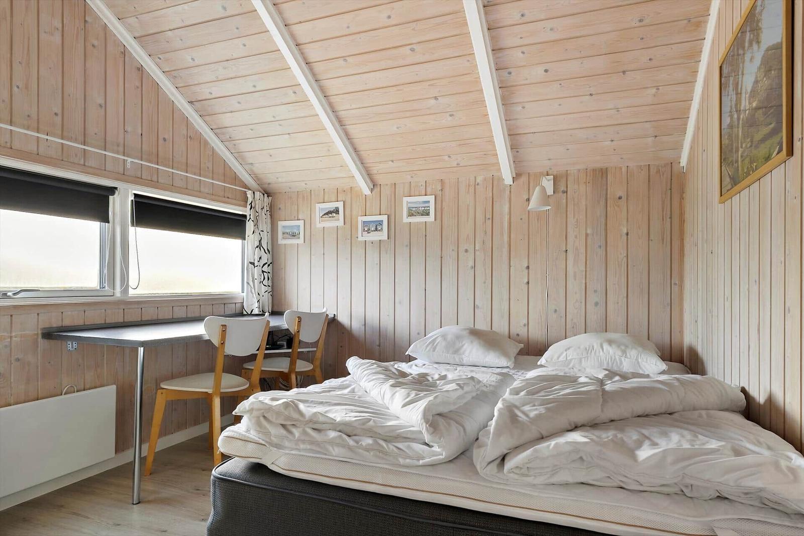 Bedroom with bed, desk, and windows. Wooden walls and ceiling.