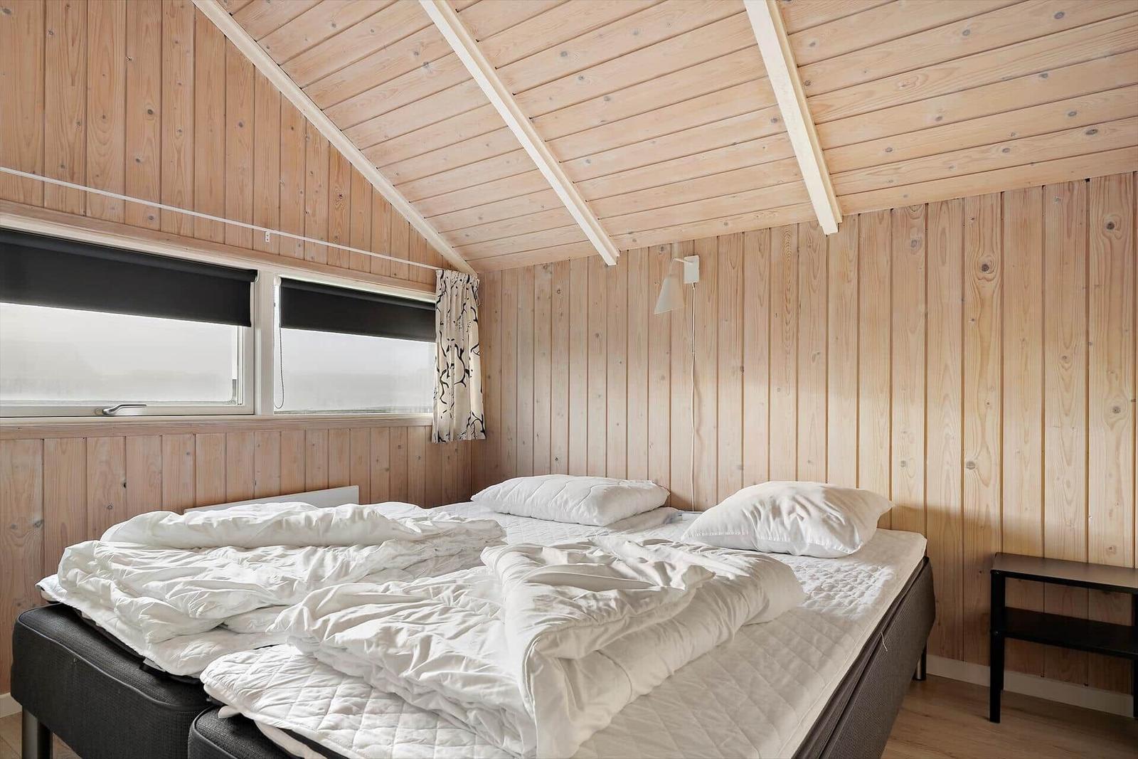 Bedroom with wooden walls and double bed under sloped ceiling.