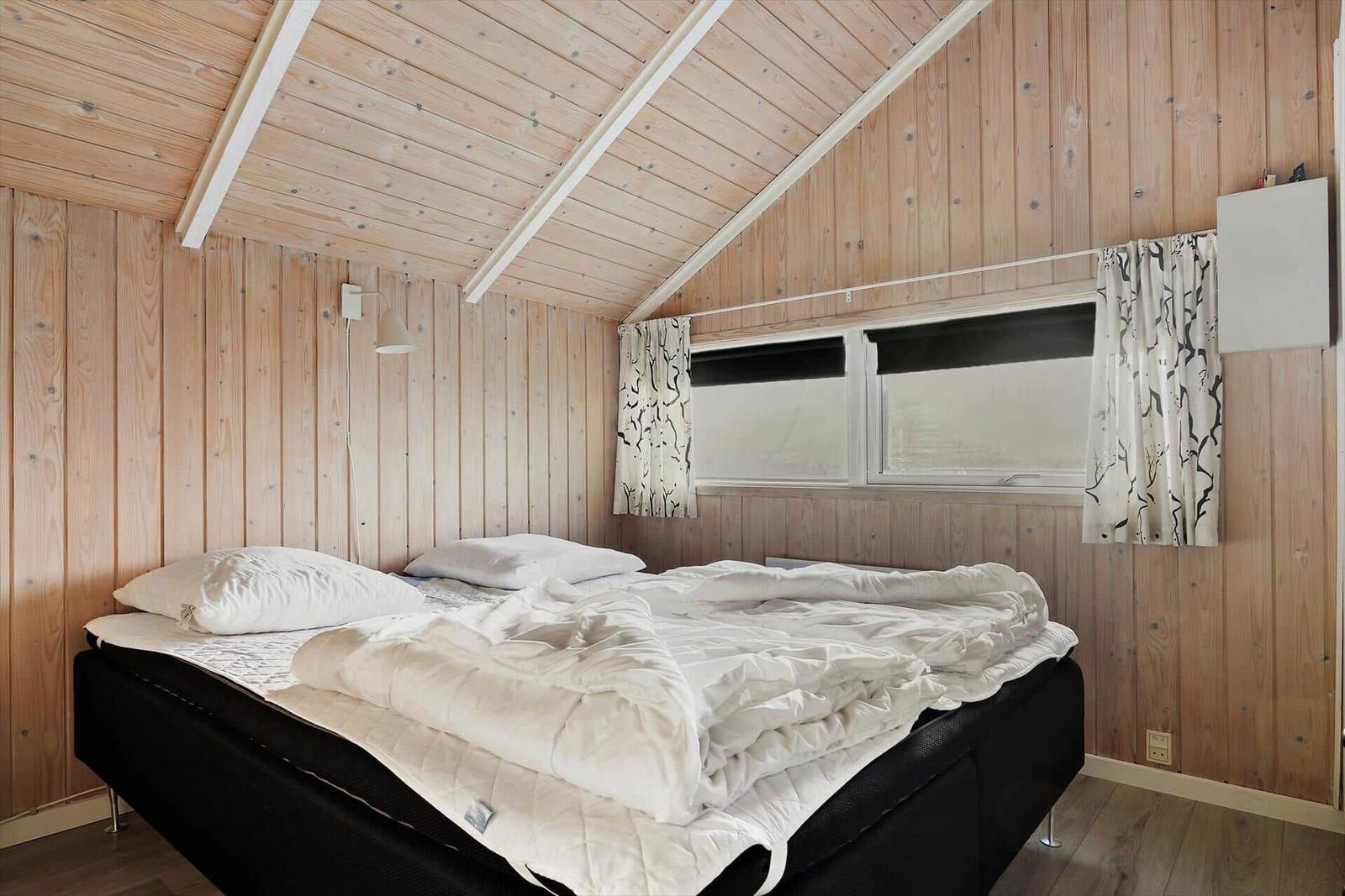 Bedroom with wooden walls and double bed under sloped ceiling.