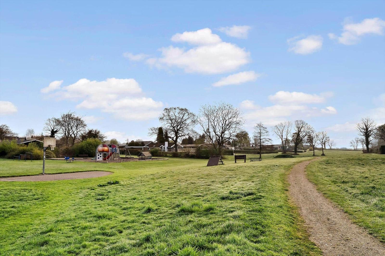 Green park with playground, basketball hoop, and path through meadows.