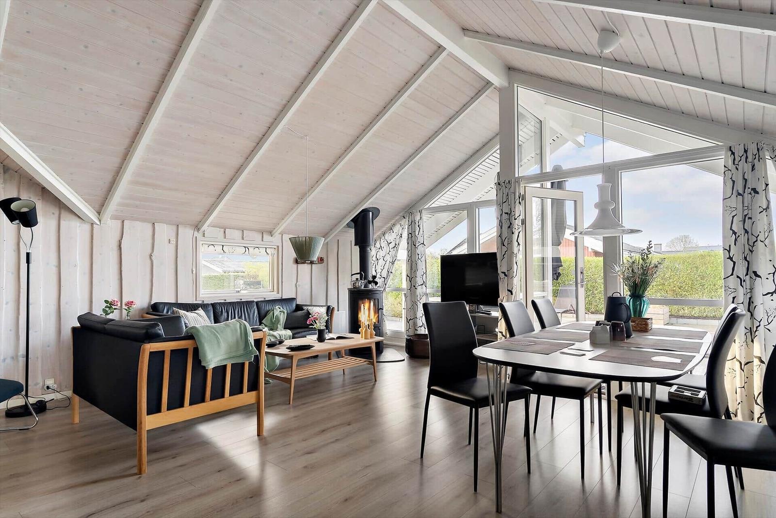 Living and dining area with wooden ceiling, fireplace, and large windows.
