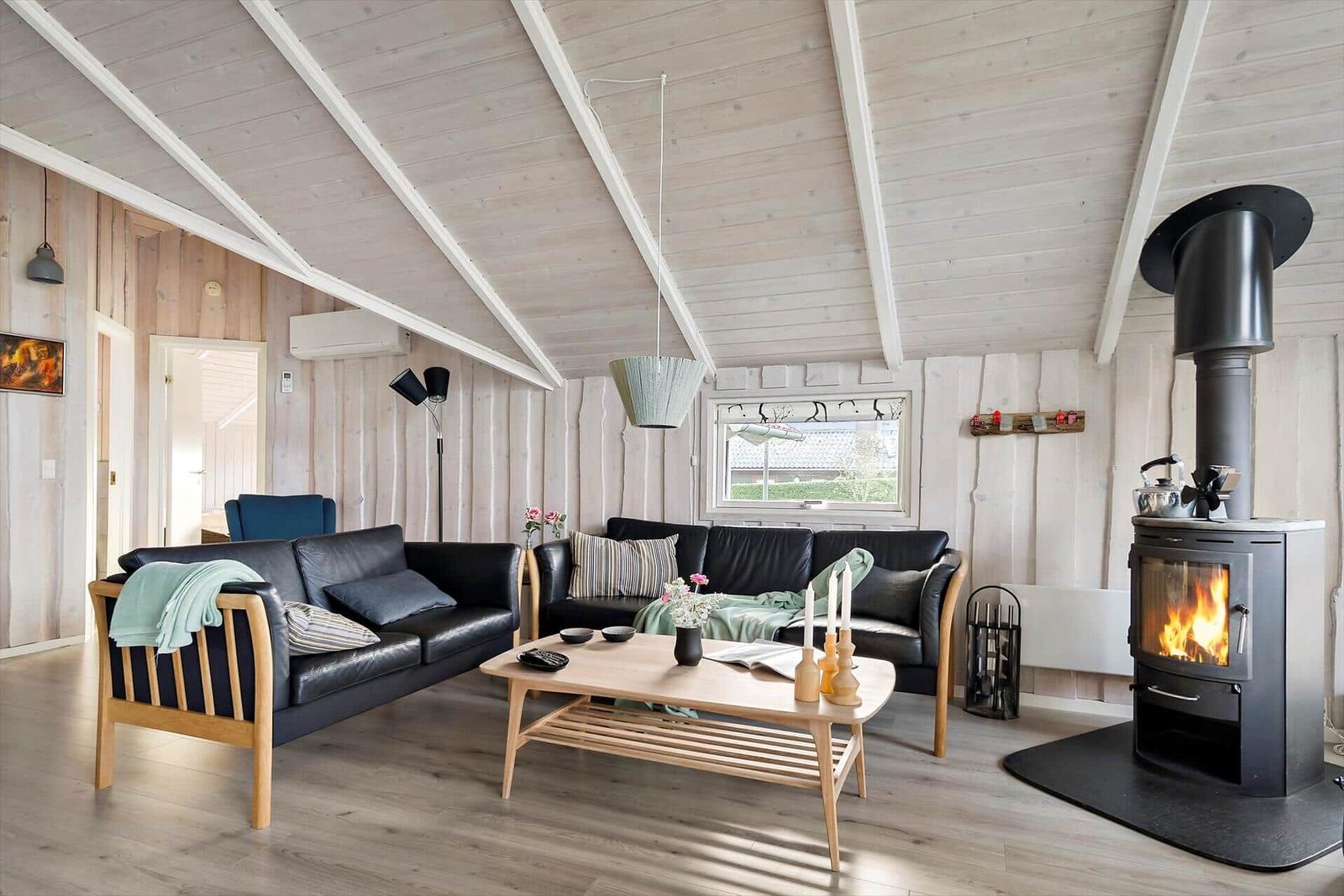 Living room with wooden ceiling, two black sofas, and wood stove.