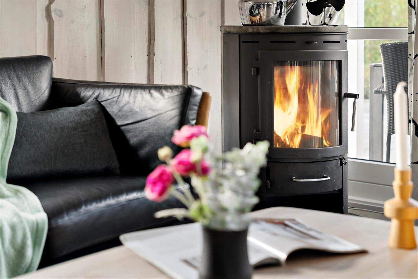 A living room with a burning wood stove, a black sofa, and a table with flowers.