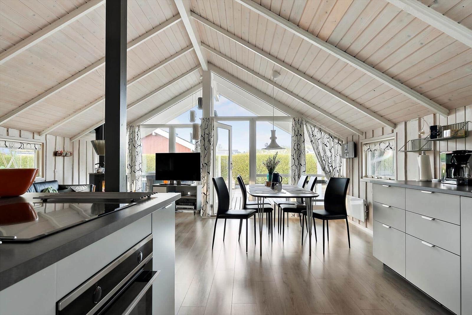 Kitchen, dining area, and living space under high ceiling with wooden roof and large windows.
