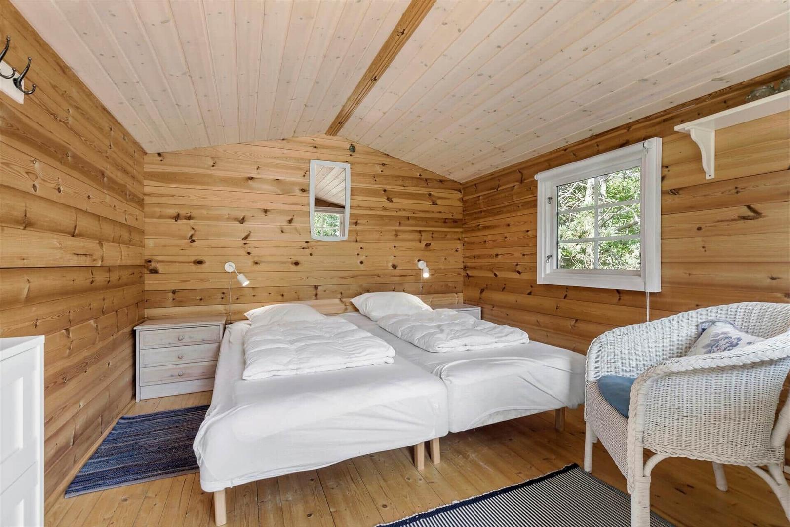 Zimmer mit zwei Betten, Holzwand und Fenster. Weiße Wicker-Sessel und Nachttisch.