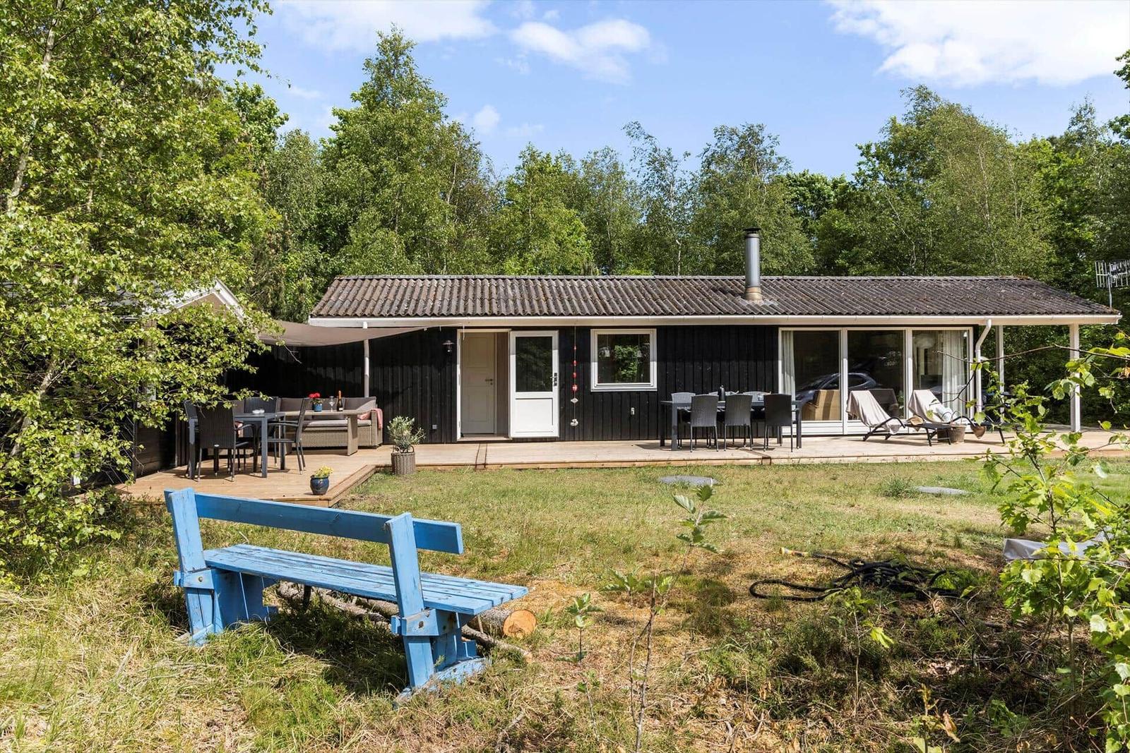 Ein schwarzes Haus mit Terrasse, Garten und blauer Bank im Vordergrund.
