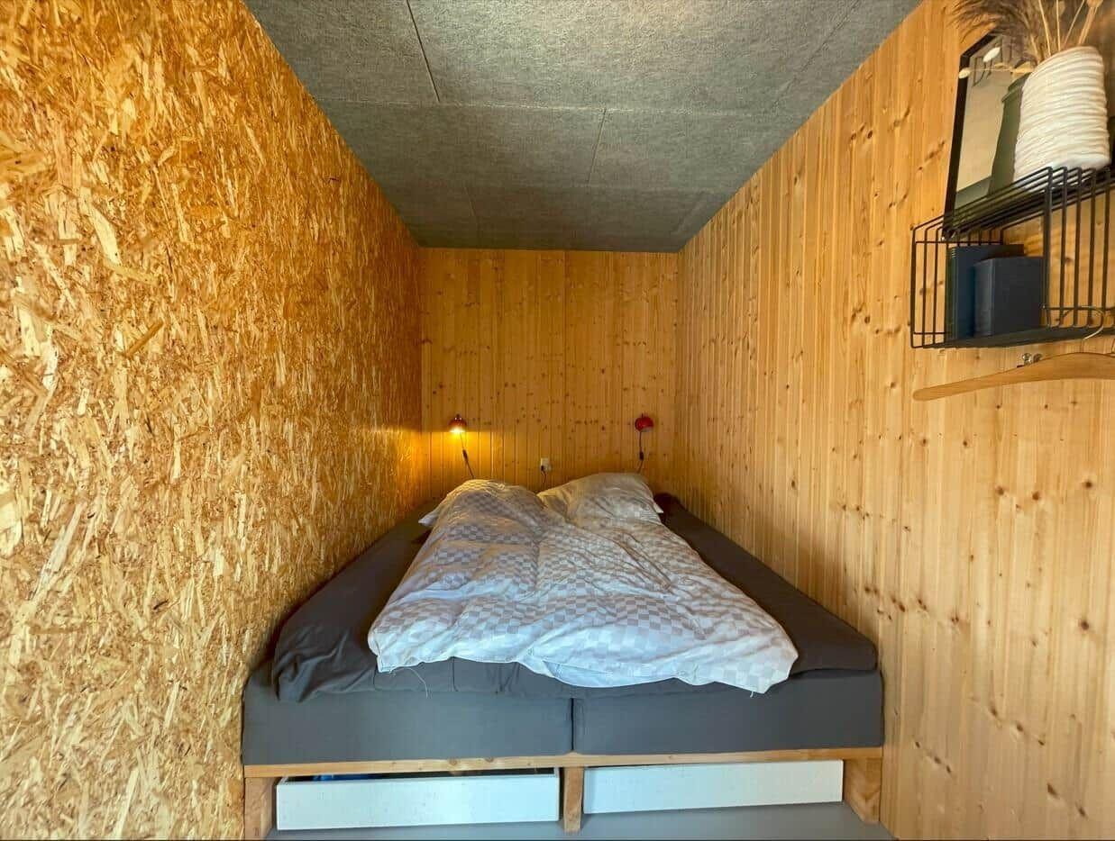 Schlafzimmer mit Bett, Holzwänden und Wandlampe.