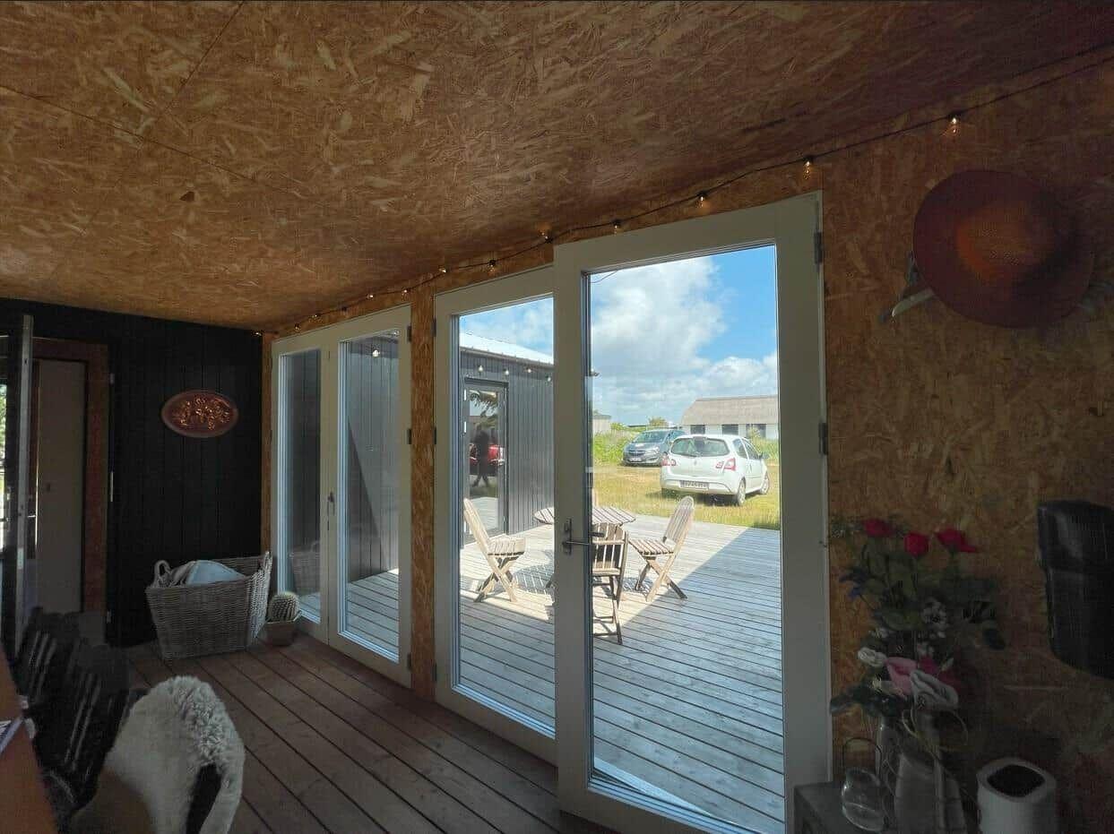 Raum mit Holzdecke und großen Glasschiebetüren auf eine Terrasse mit Tisch und Stühlen.