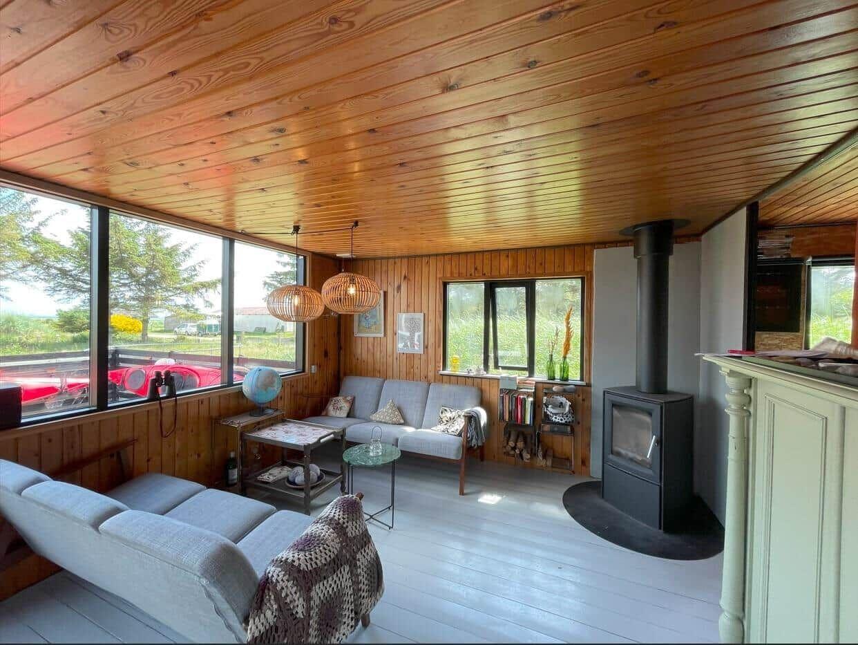 Wohnzimmer mit Holzdecke, Sofa, Kamin und großen Fenstern.