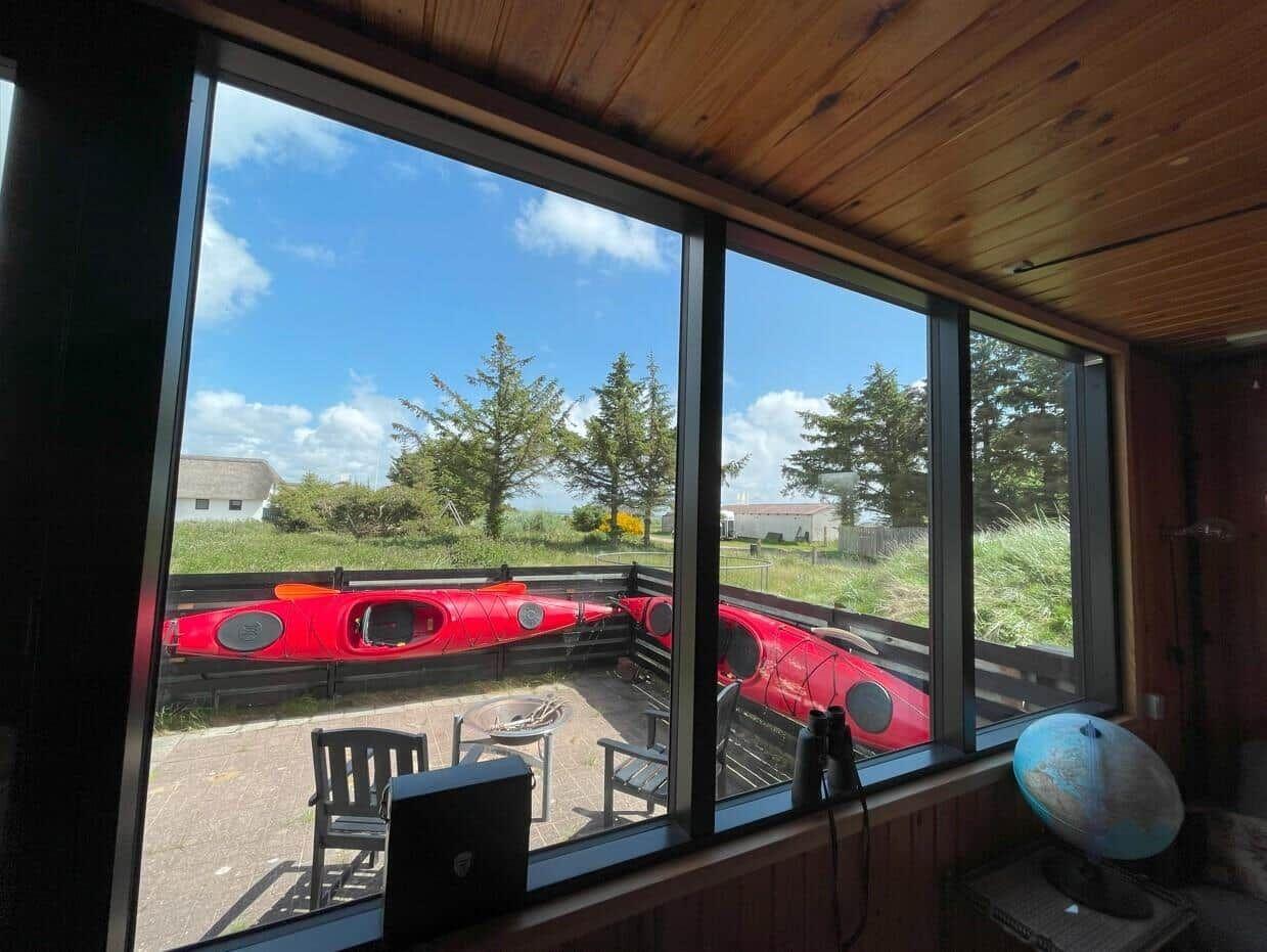 Durch große Fenster blickt man auf zwei rote Kanus und einen Garten.