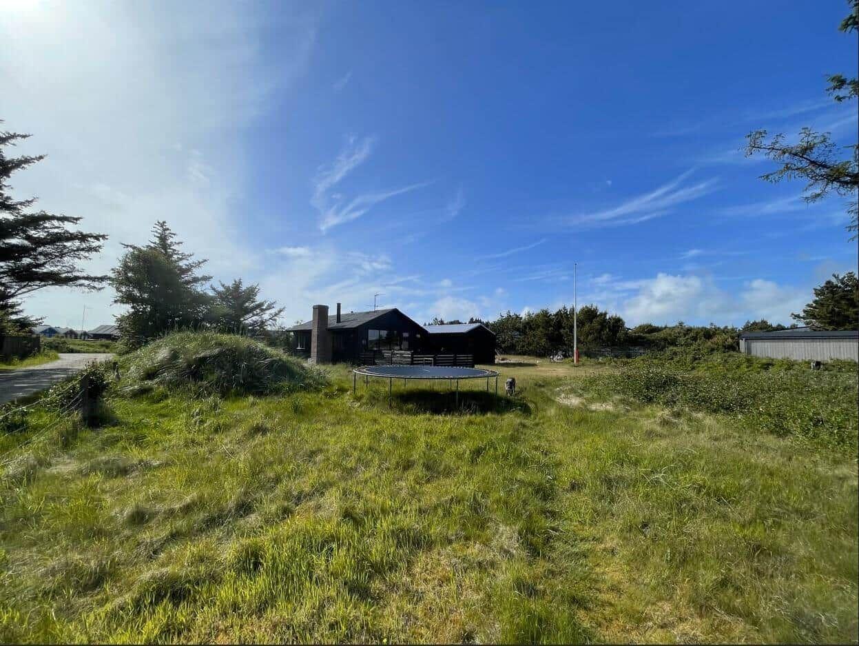 Ein Haus mit Trampolin in grünem Gelände unter blauem Himmel.
