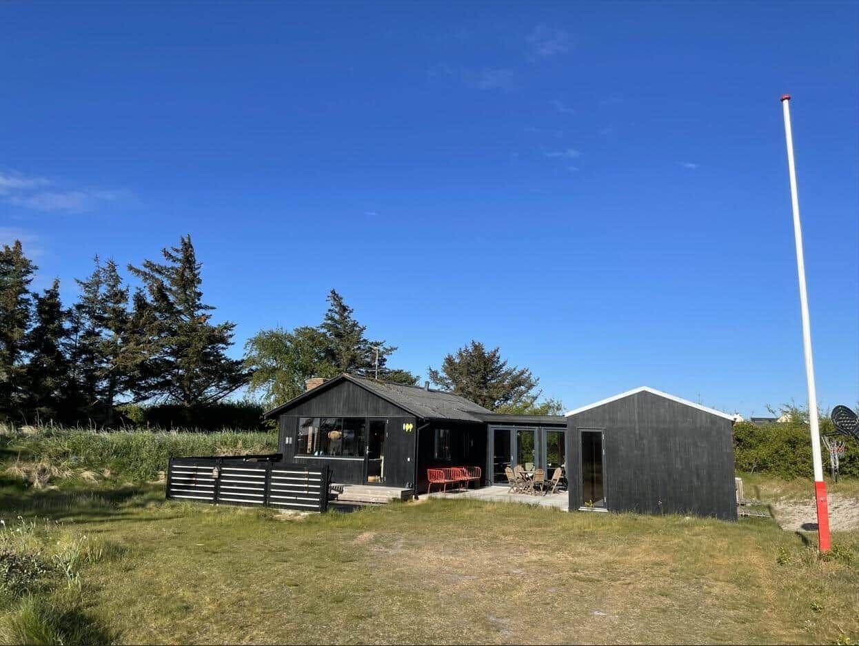 Schwarzes Ferienhaus mit Terrasse und Garten unter blauem Himmel.