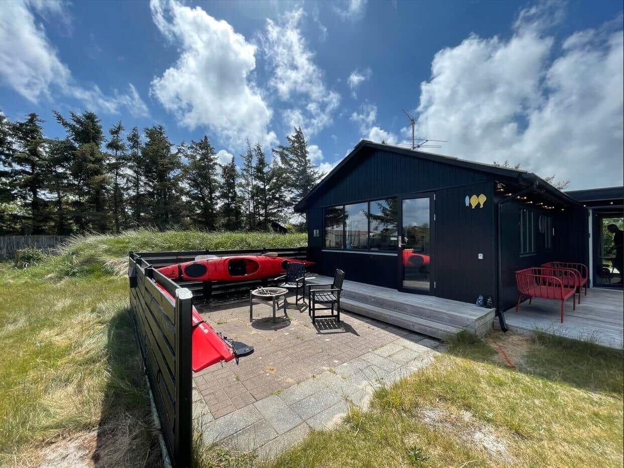 Schwarzes Haus mit Terrasse, roten Stühlen und Kajak auf dem Hof.