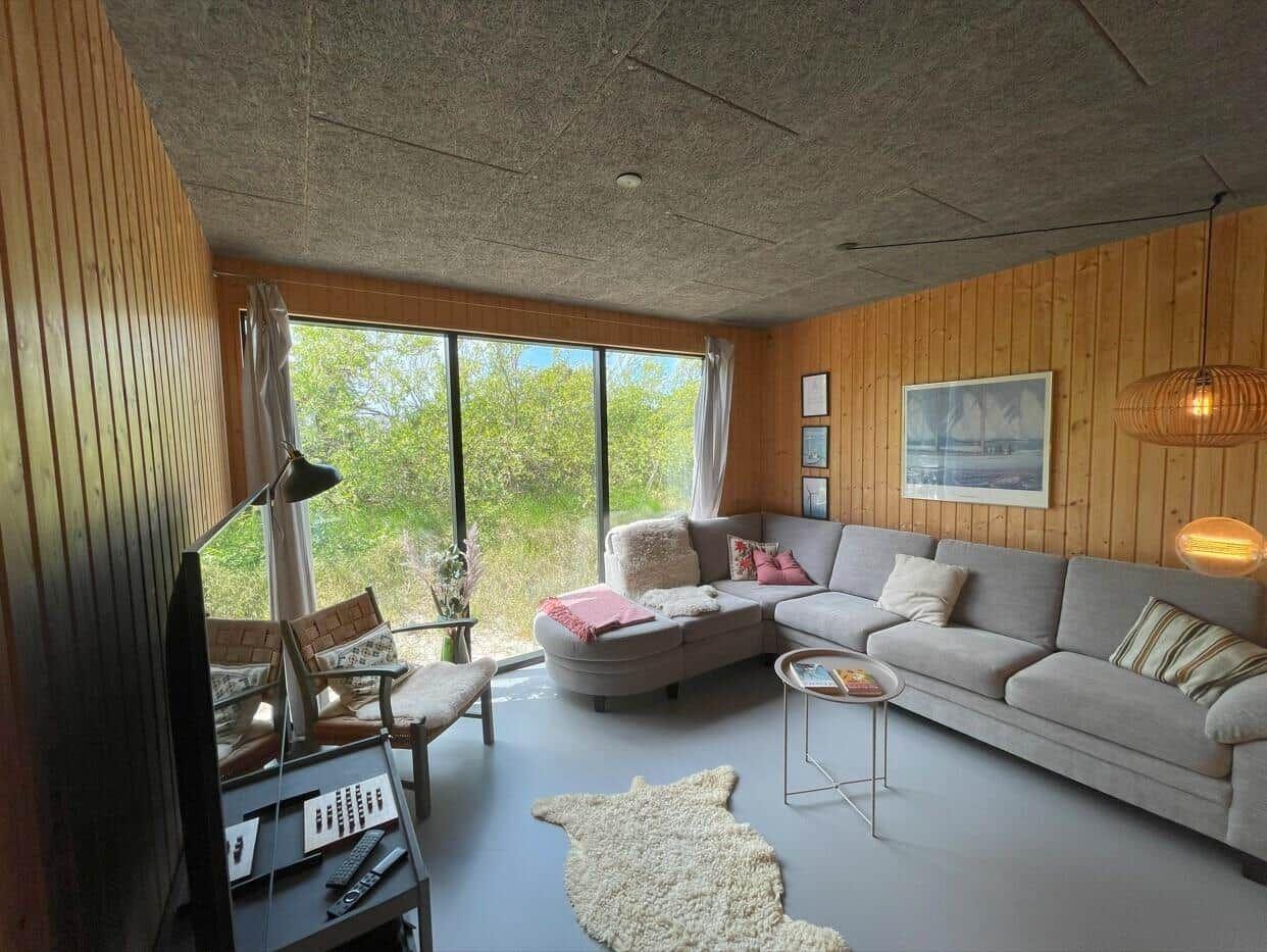 Wohnzimmer mit Sofa, Fenster und Holzwand.