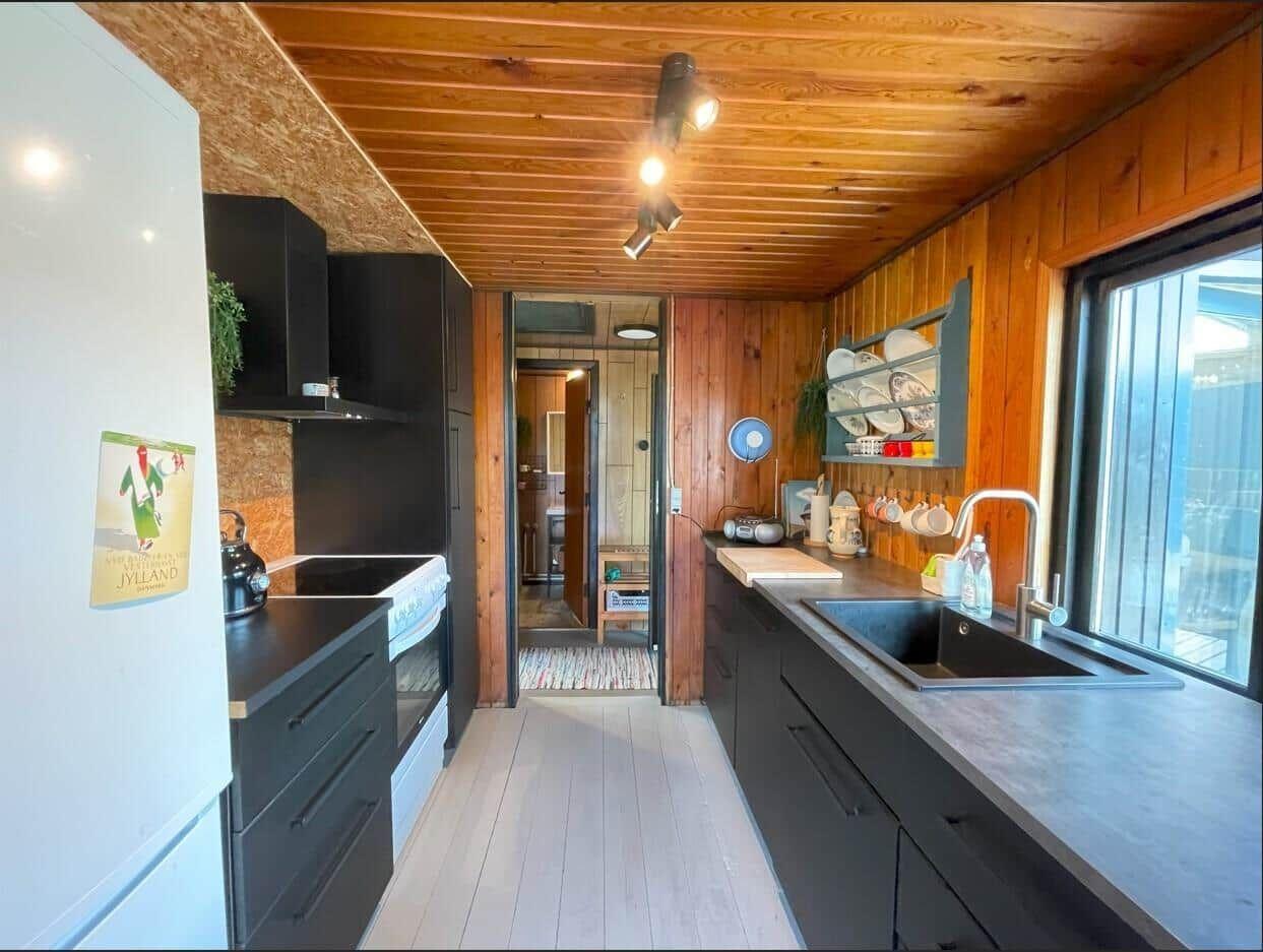 Küche mit Holzwänden, schwarzen Schränken und Fensterblick.