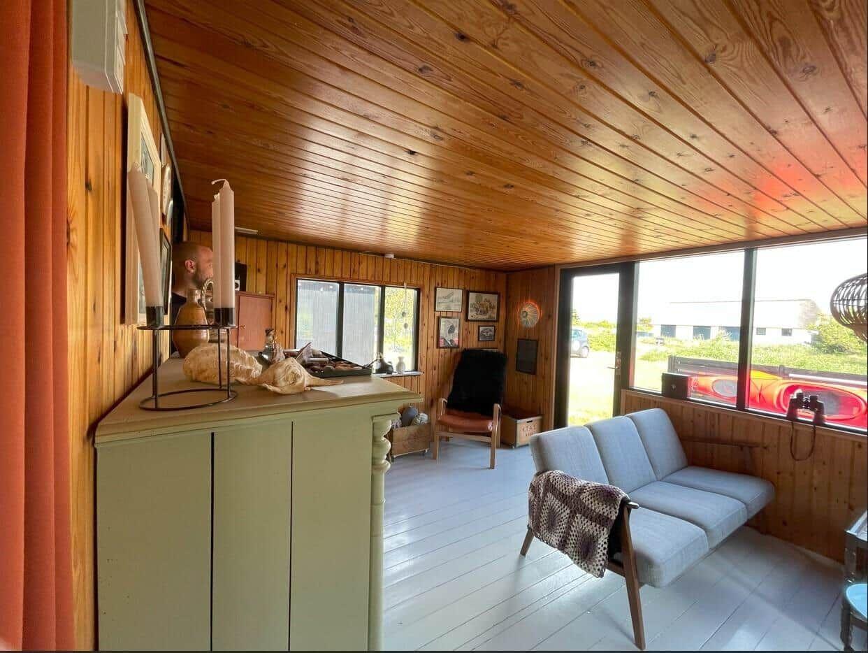 Wohnraum mit Holzwand und -decke, Sofa, Fenster und Schrank.