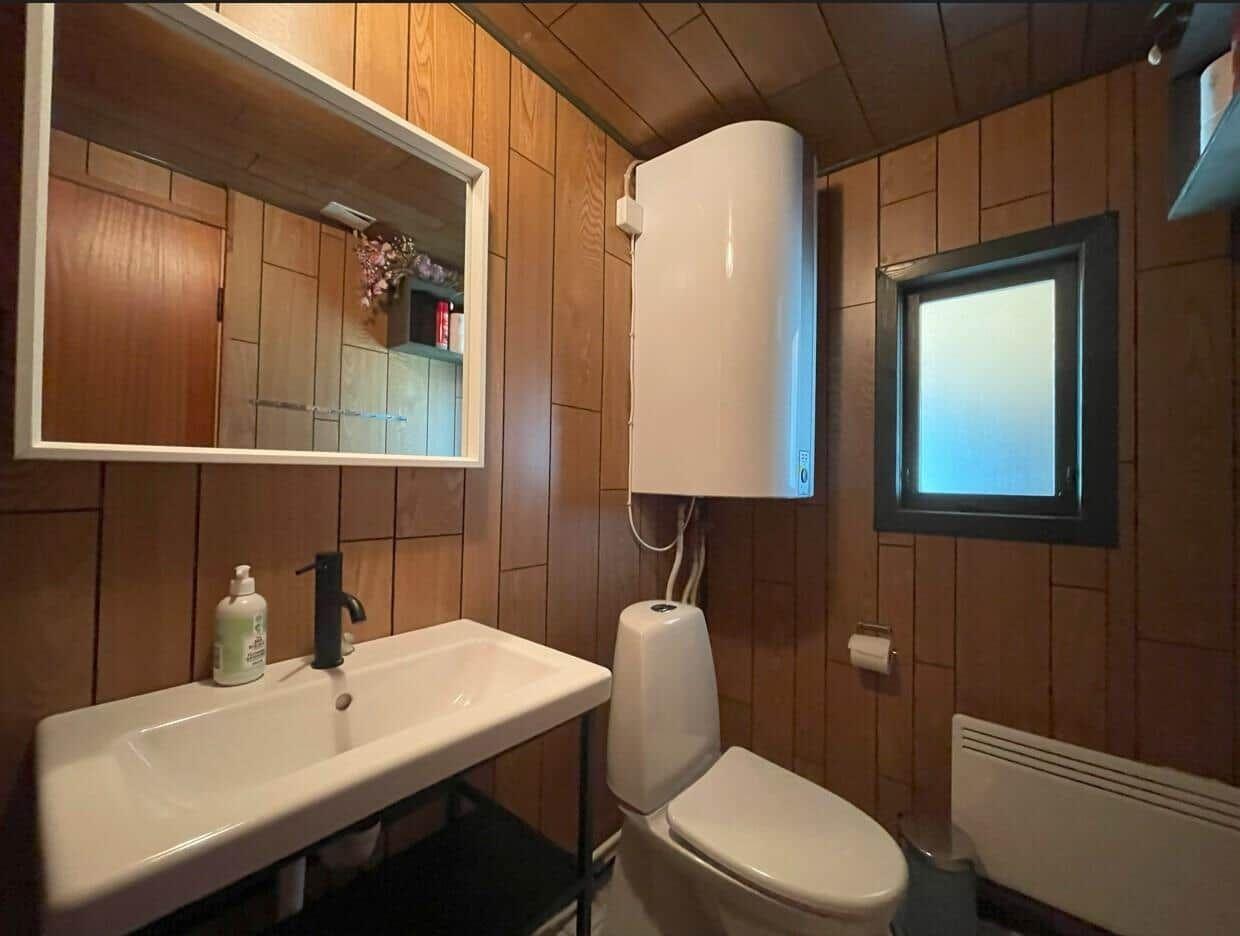 Badezimmer mit Waschbecken, Toilette und Spiegel an Holzwand