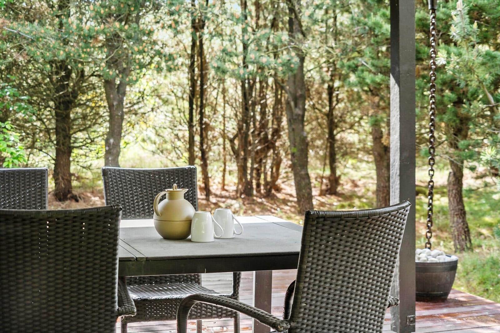 Terrasse mit Tisch und Stühlen im Wald. Auf dem Tisch stehen Teekanne und Tassen.