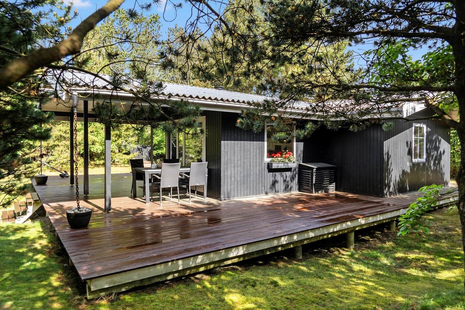 Schwarze Holzhütte mit Terrasse und Garten. Tisch und Stühle auf der Veranda.
