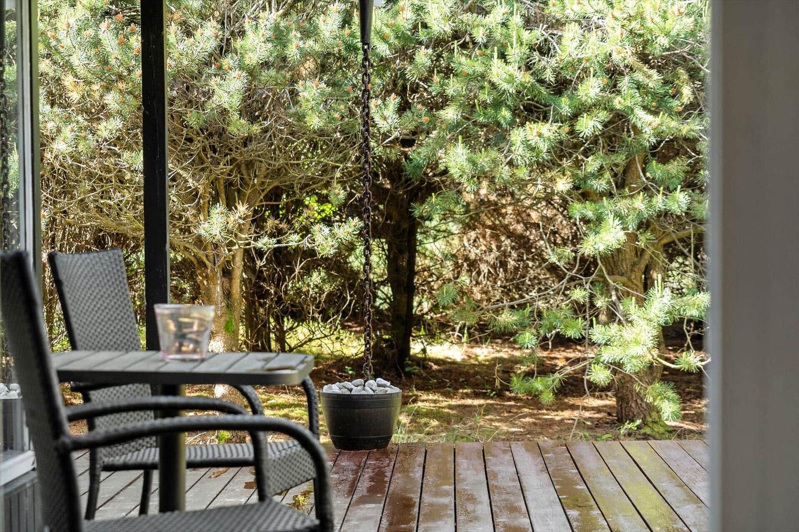 Terrasse mit Tisch, Stühlen und Hängesitz vor grüner Hecke.