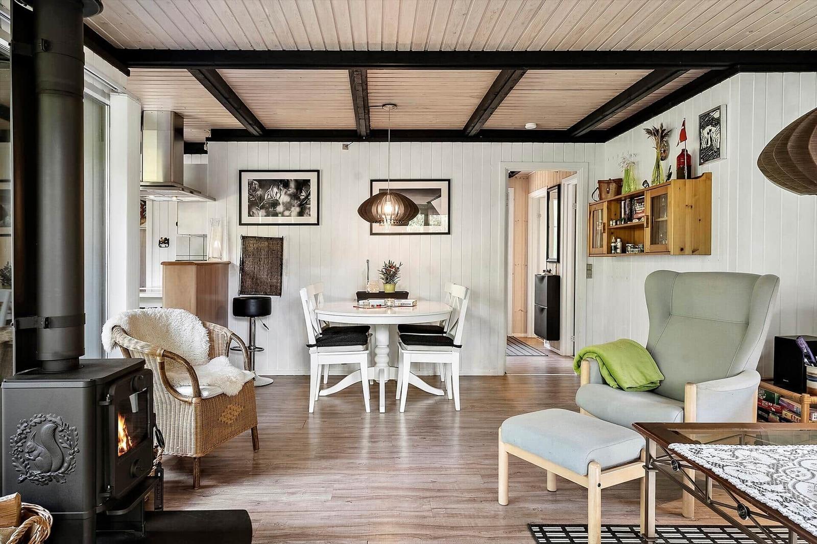 Wohnzimmer mit Esstisch, Sessel und Kaminofen. Holzboden und weiße Wände.