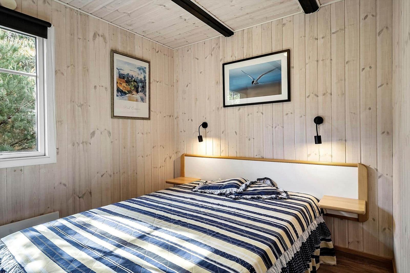 Schlafzimmer mit Holzwand, Bett und Fenster mit Blick auf Bäume.