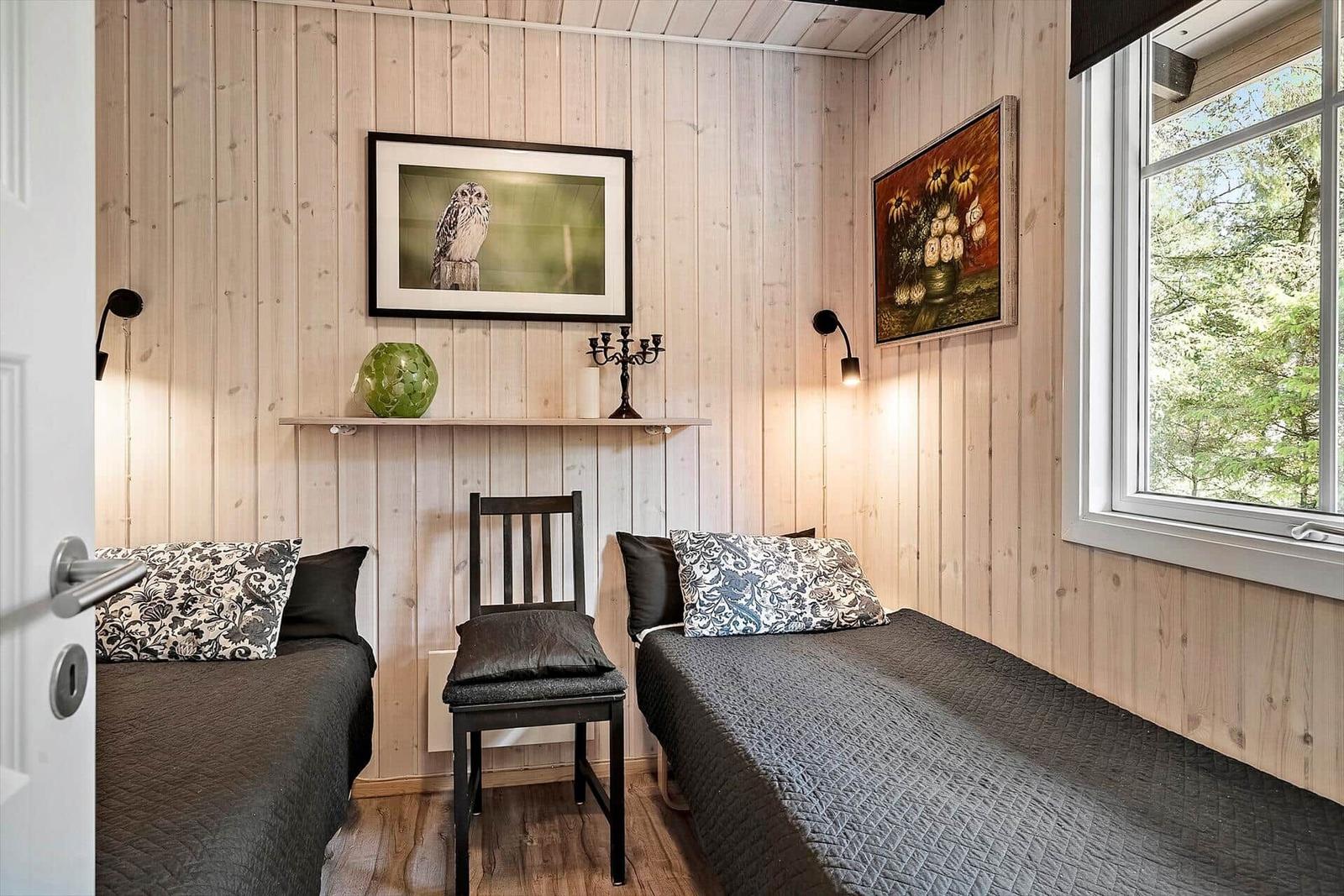 Zwei Betten, Holzwand, Fenster mit Blick auf Wald, Wandbild und Stuhl.