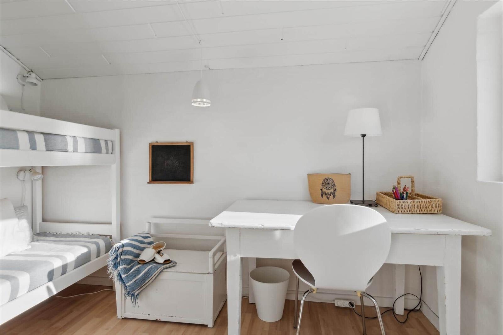 A room with bunk bed, desk and chair. Wall with chalkboard and lamps.