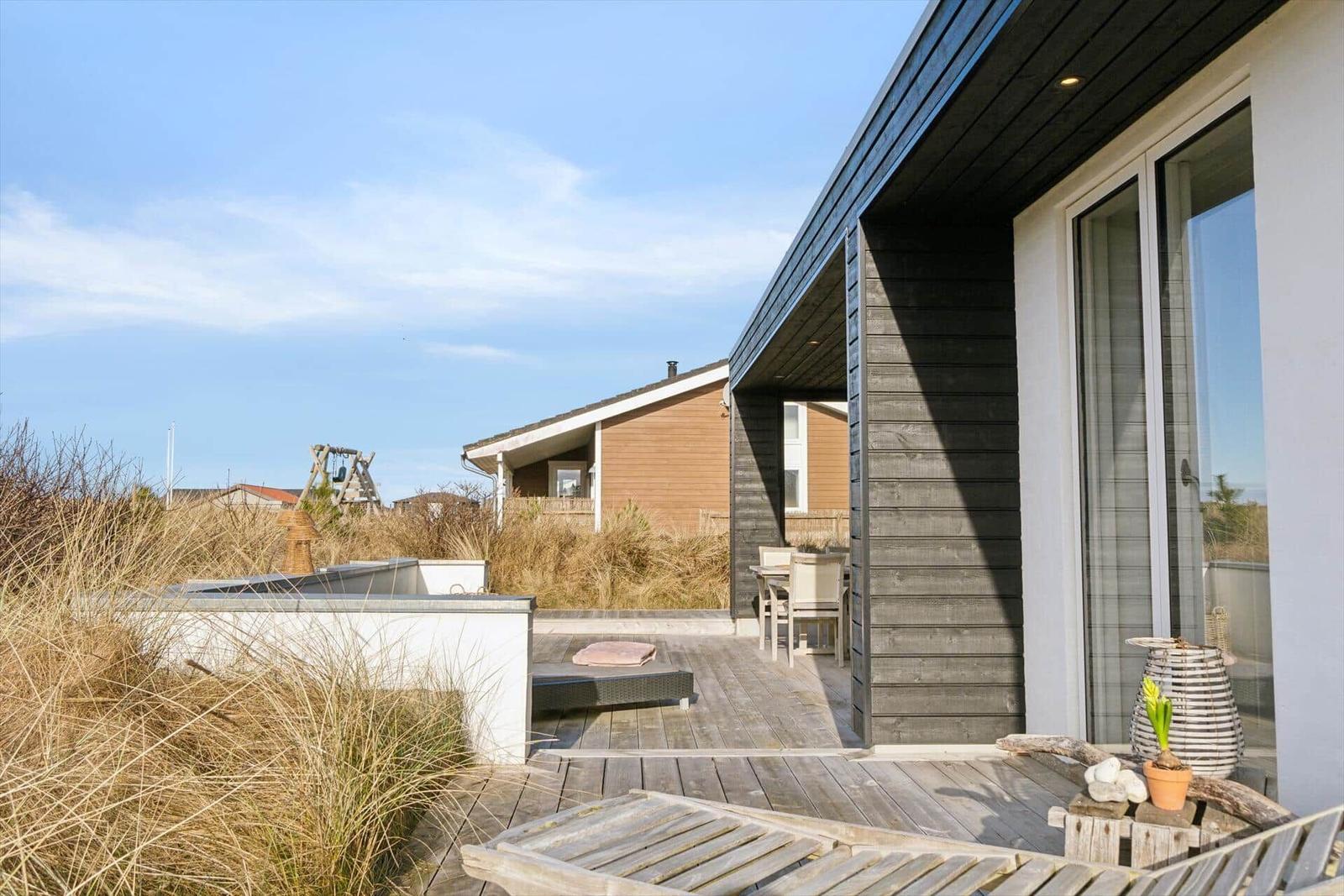 Deck with lounge, table, and chairs. Background: dunes and vacation home.