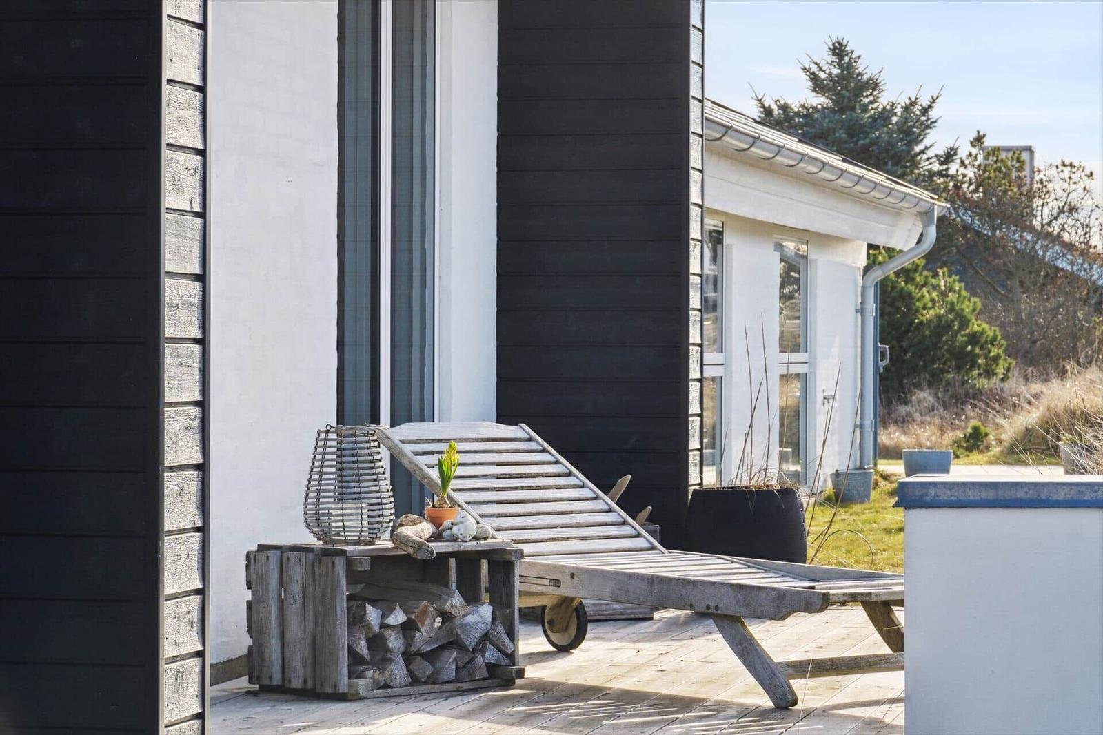 Deck with lounge chair and firewood stack in front of modern house
