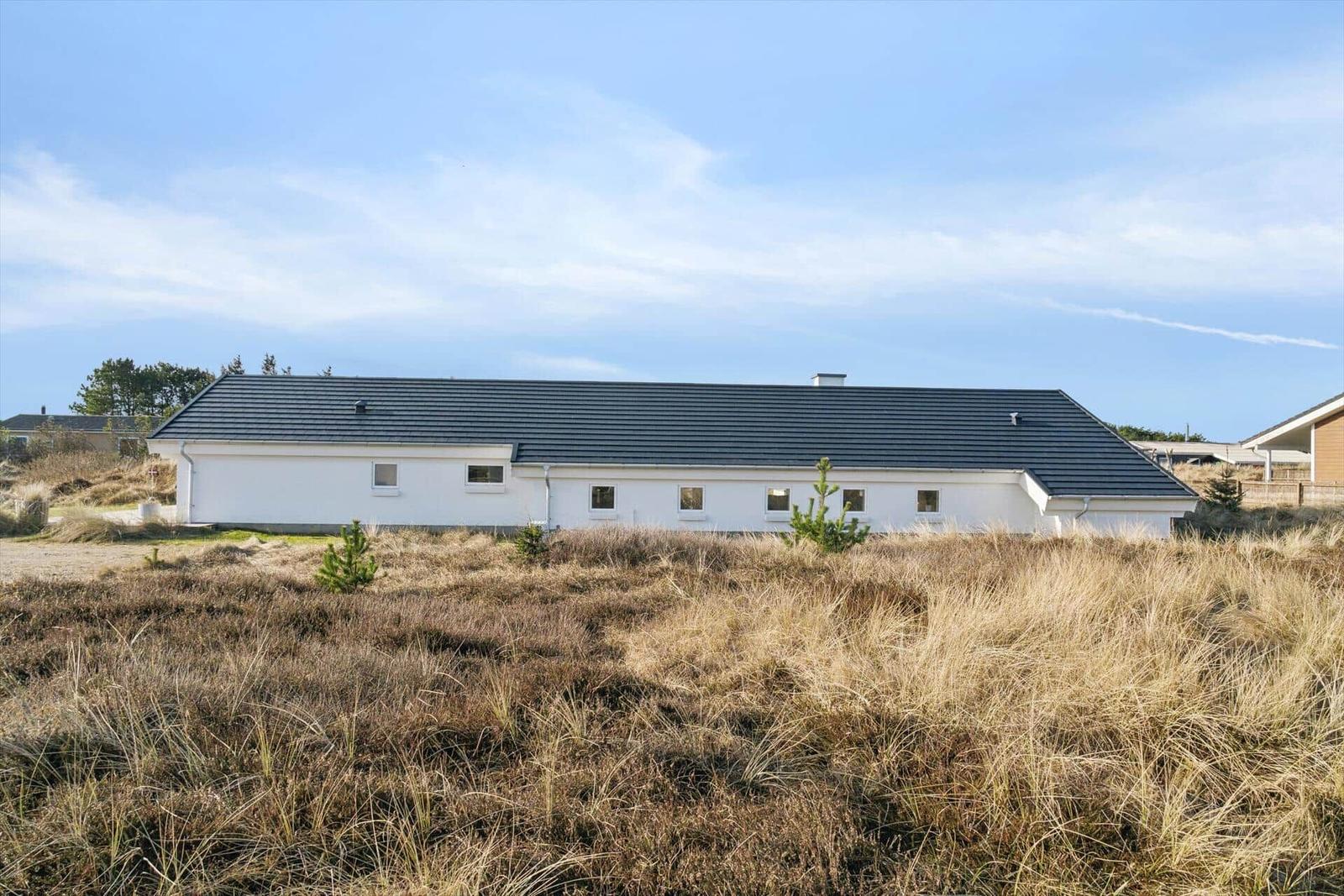 A white house with a dark roof sits in a grassy landscape under a blue sky.