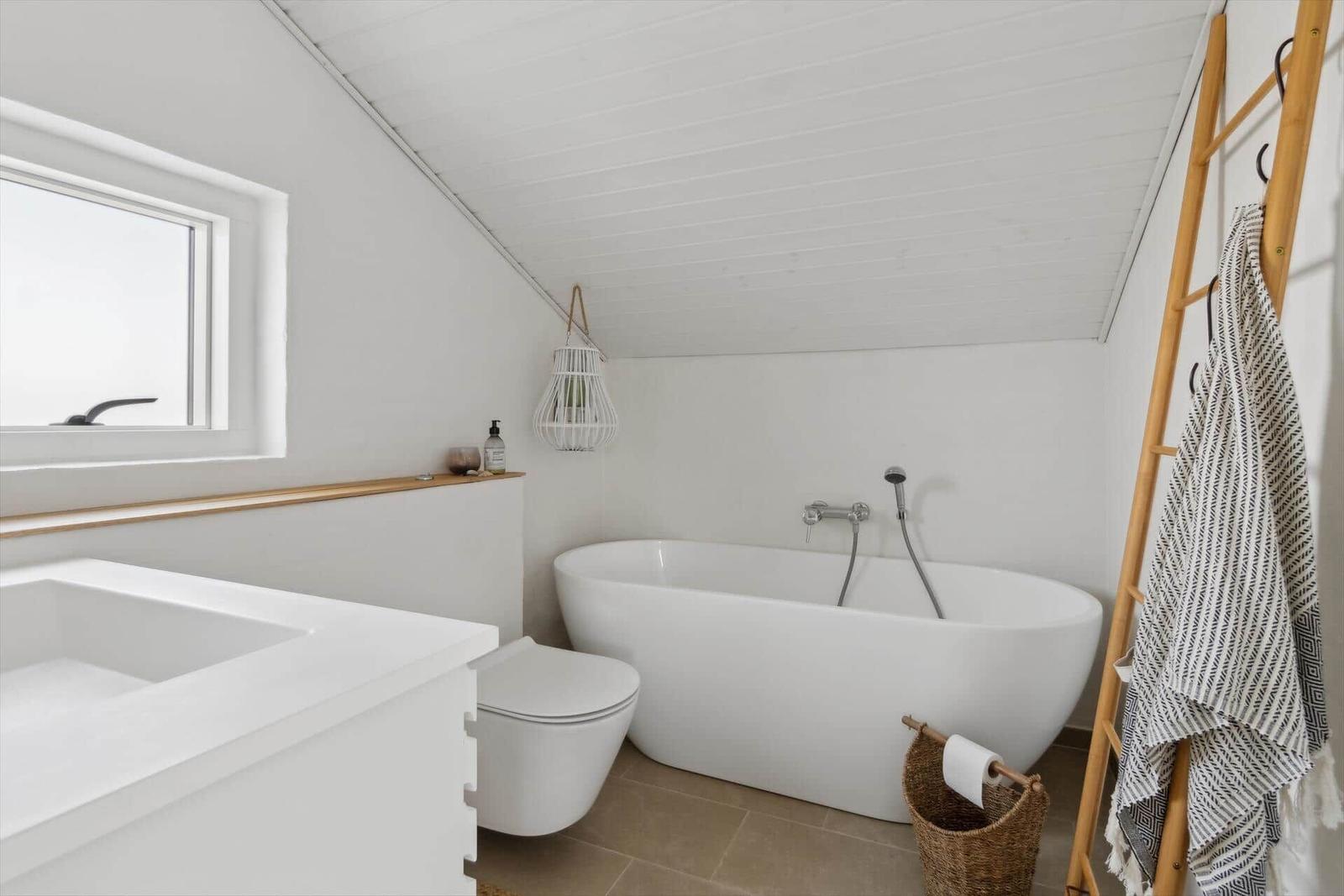 Bathroom with freestanding bathtub, toilet, and sink under sloped ceiling.