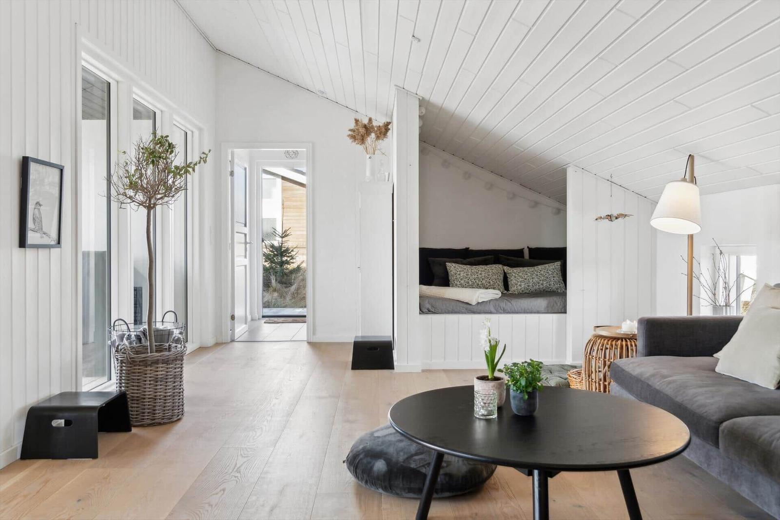 Living area with sleeping nook, sofa, and table. Wooden floor and white walls.