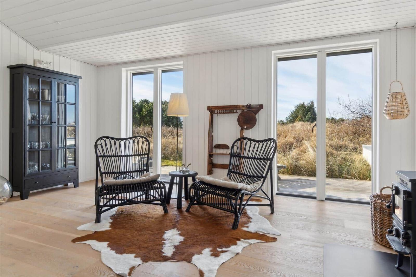 Two black rattan chairs sit on a cowhide rug near large windows.