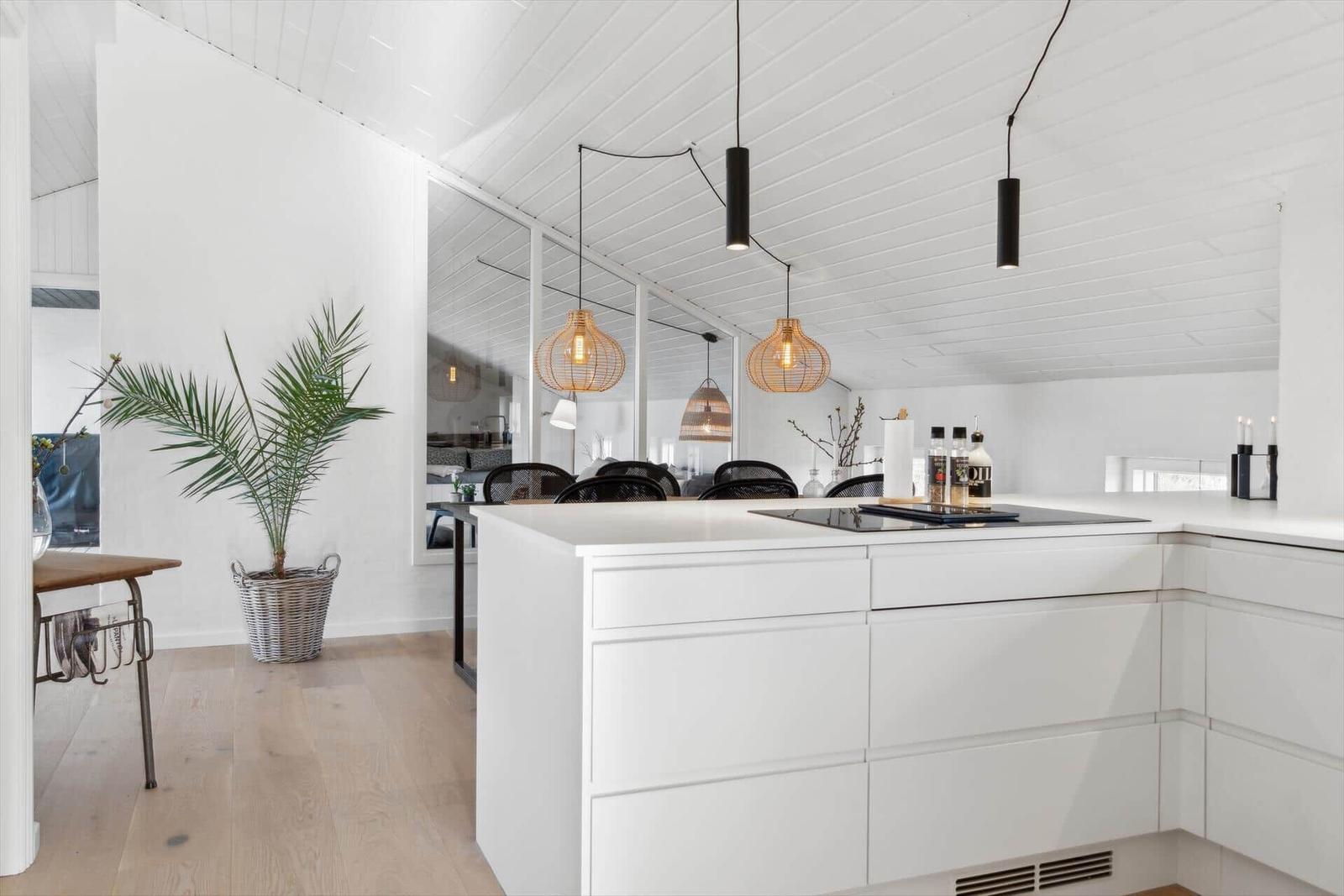 Modern kitchen with white cabinets and kitchen island. Hanging lamps and plant are visible.