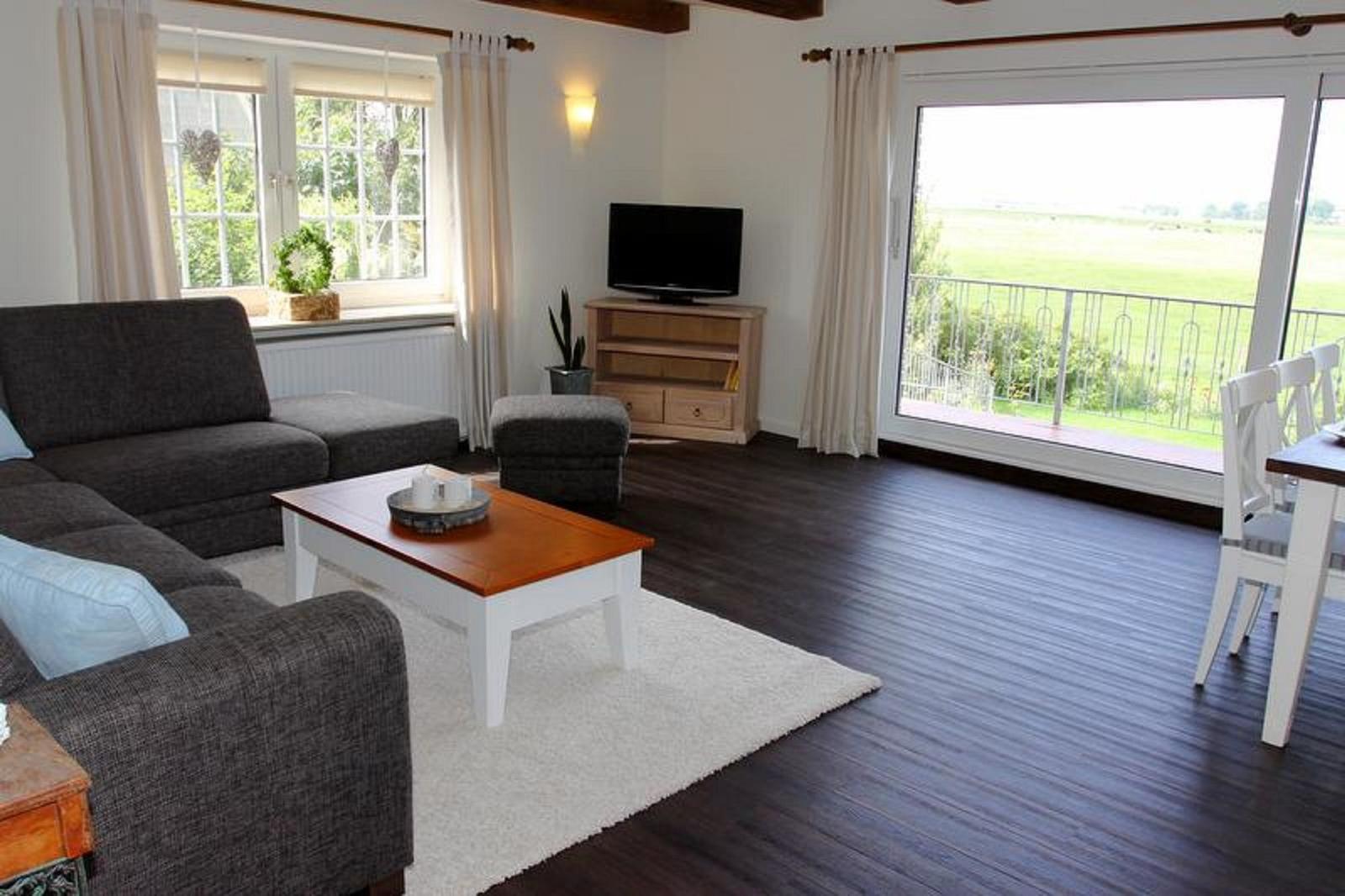 Wohnzimmer mit Sofa, Couchtisch und TV. Balkon mit Blick auf Feld.