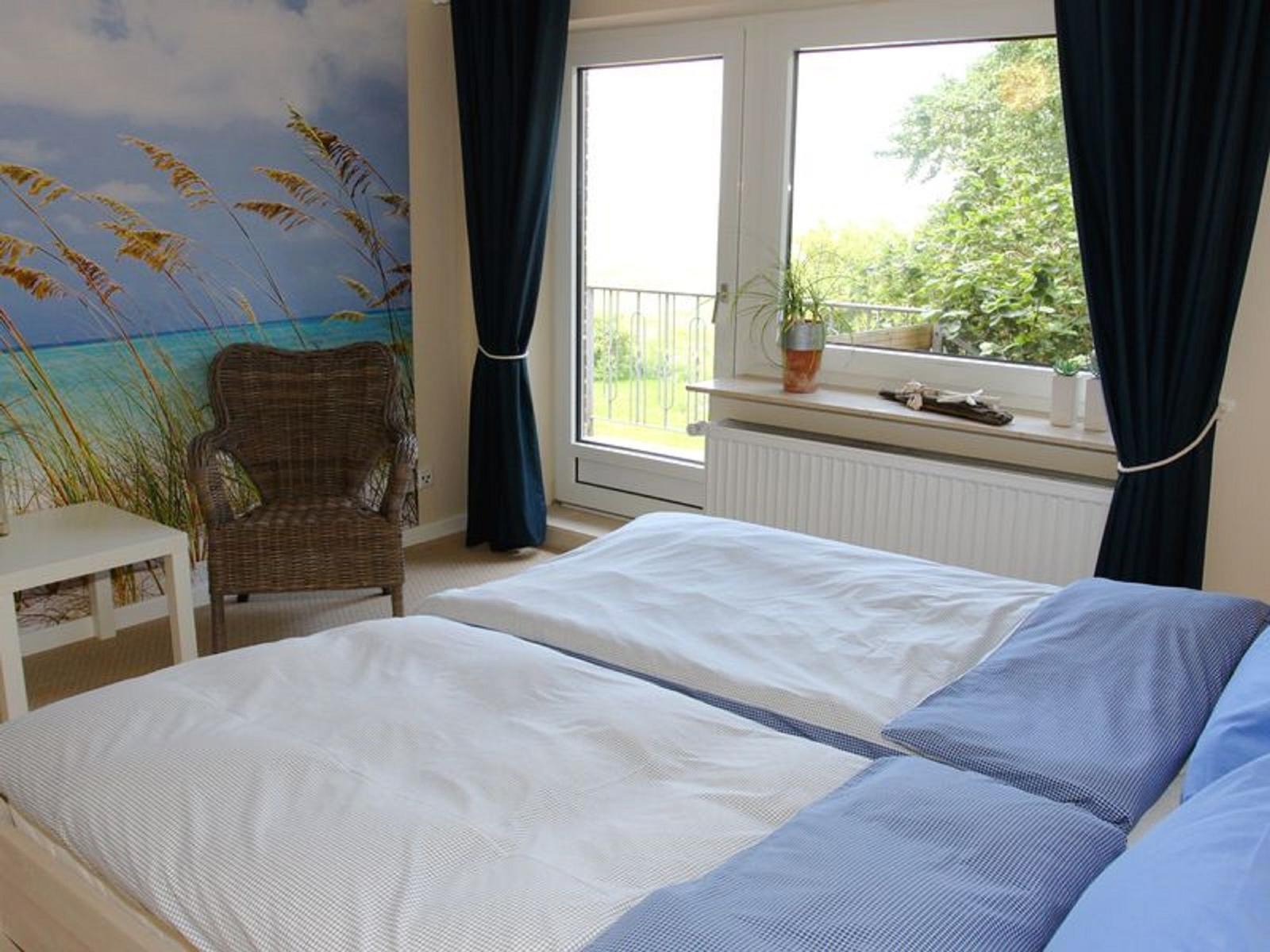 Schlafzimmer mit Bett, Stuhl und Fenster zur Terrasse.