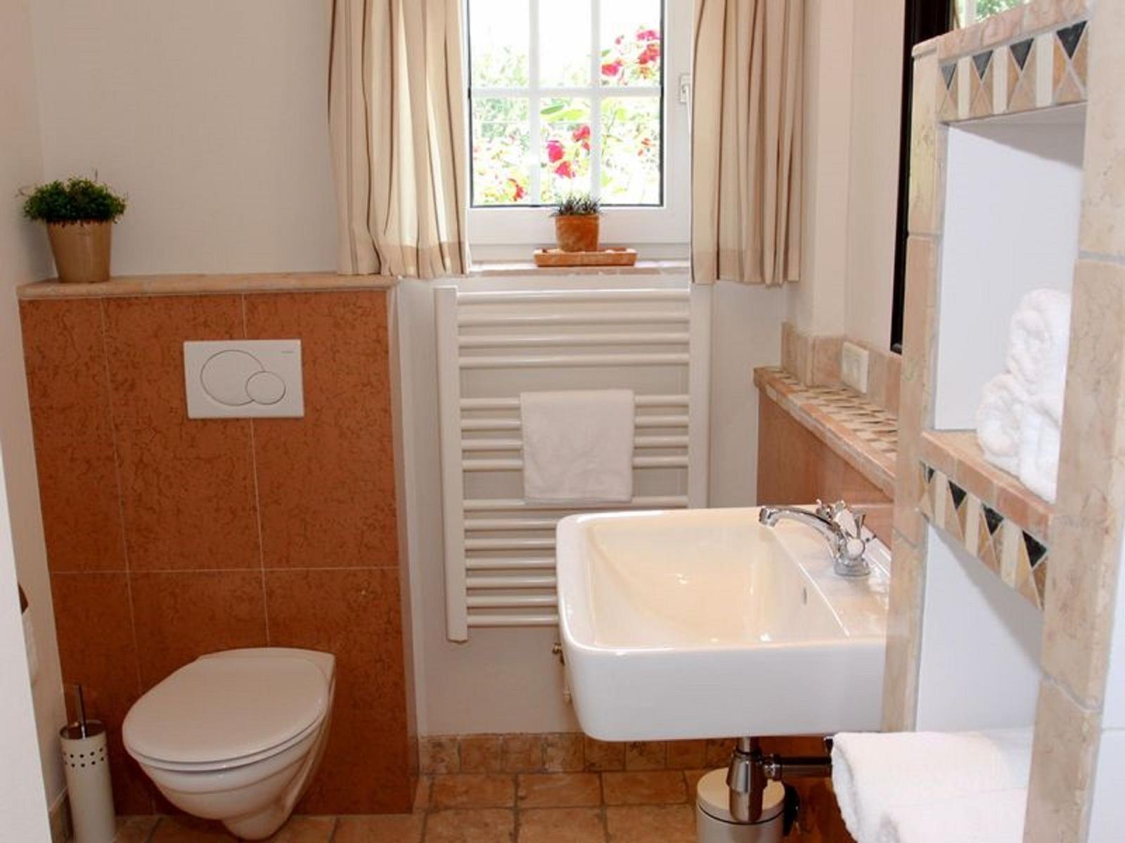 Badezimmer mit Toilette, Waschbecken und Fenster mit Blick auf Garten.