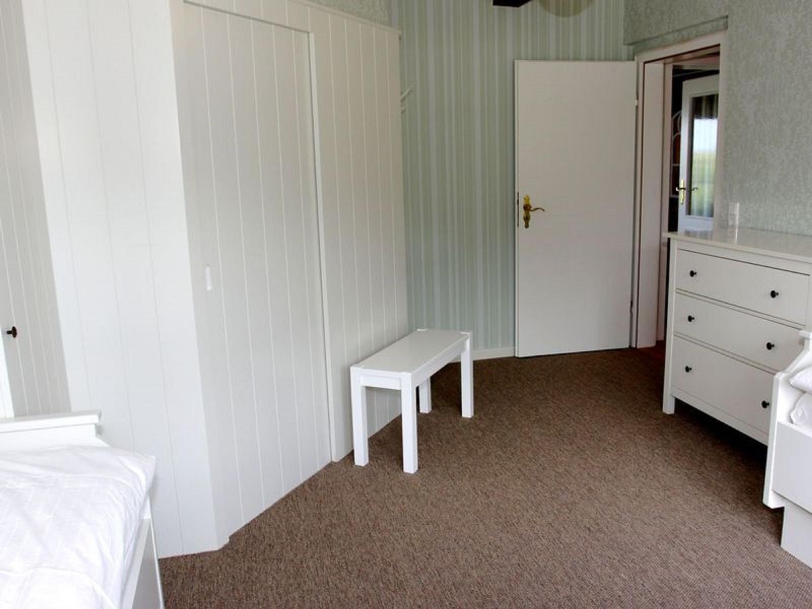 Schlafzimmer mit weißer Bettbank, Schrank und Schrank mit Schubladen.