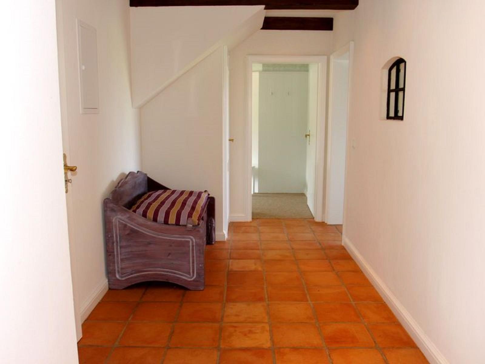 Flur mit Terrakottboden, Sitzbank und Holzbalken an der Decke.