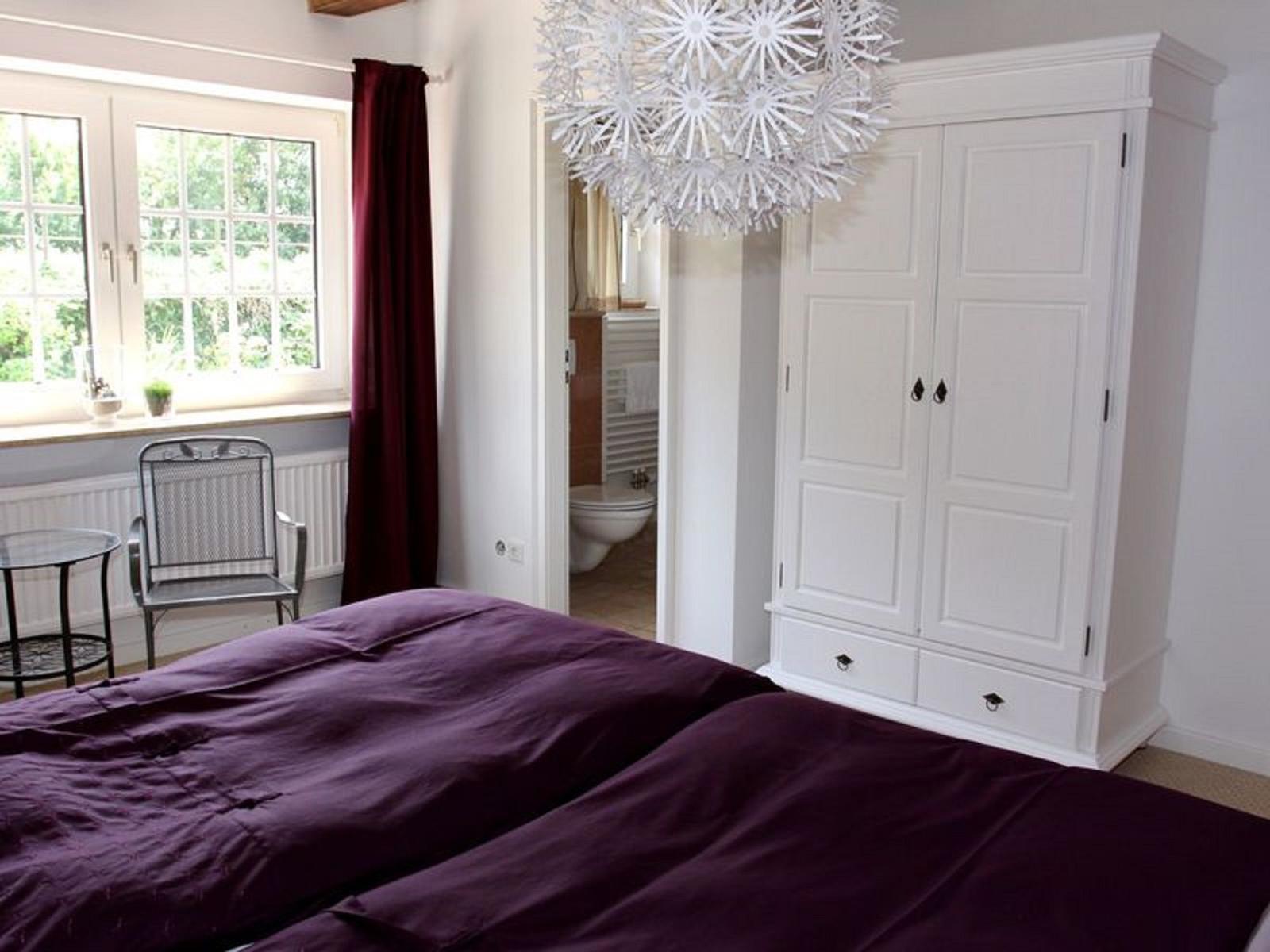 Schlafzimmer mit Doppelbett, weißem Schrank und Fenster mit Blick auf Garten.