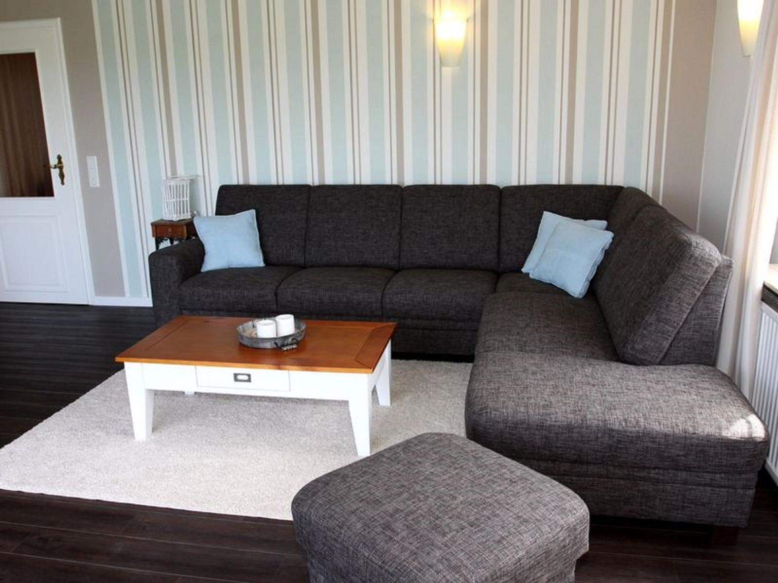 Ein Wohnzimmer mit grauem Sofa, Holztisch und Streifenwand.