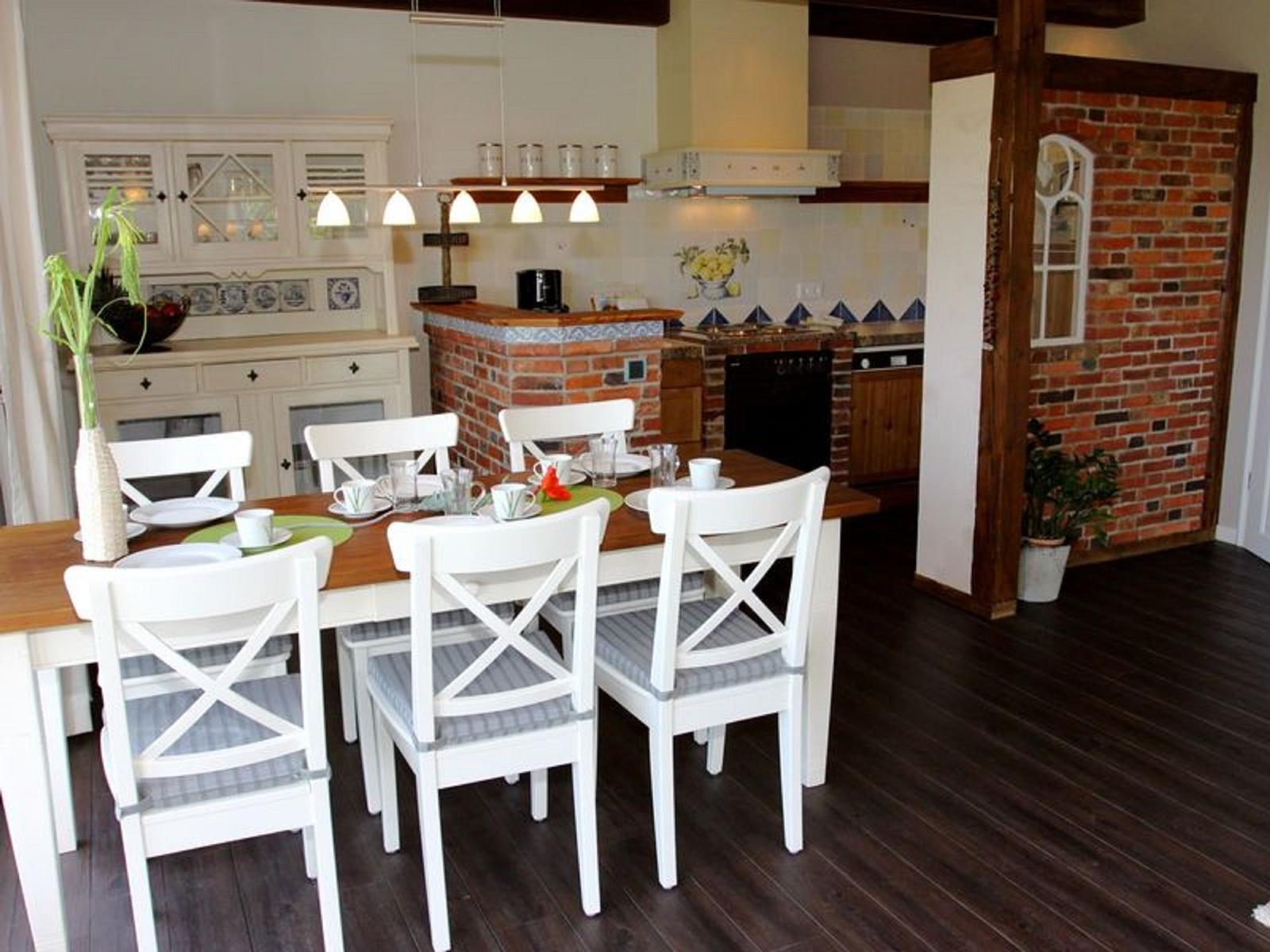 Esszimmer mit Tisch, Stühlen und Küchenbereich mit Backsteinwand.