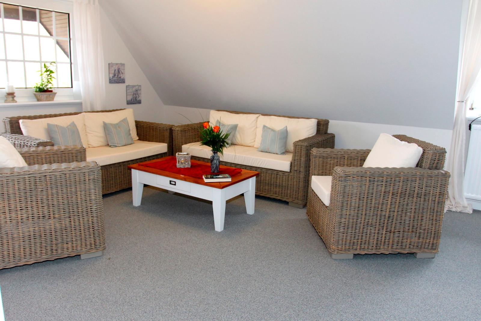 Wohnzimmer mit Rattanmöbeln, weißem Tisch und Blumen.