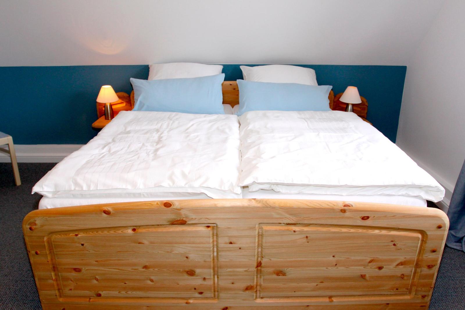 Doppelbett mit Holzrahmen, weißen Bettwäsche und blauen Kissen.